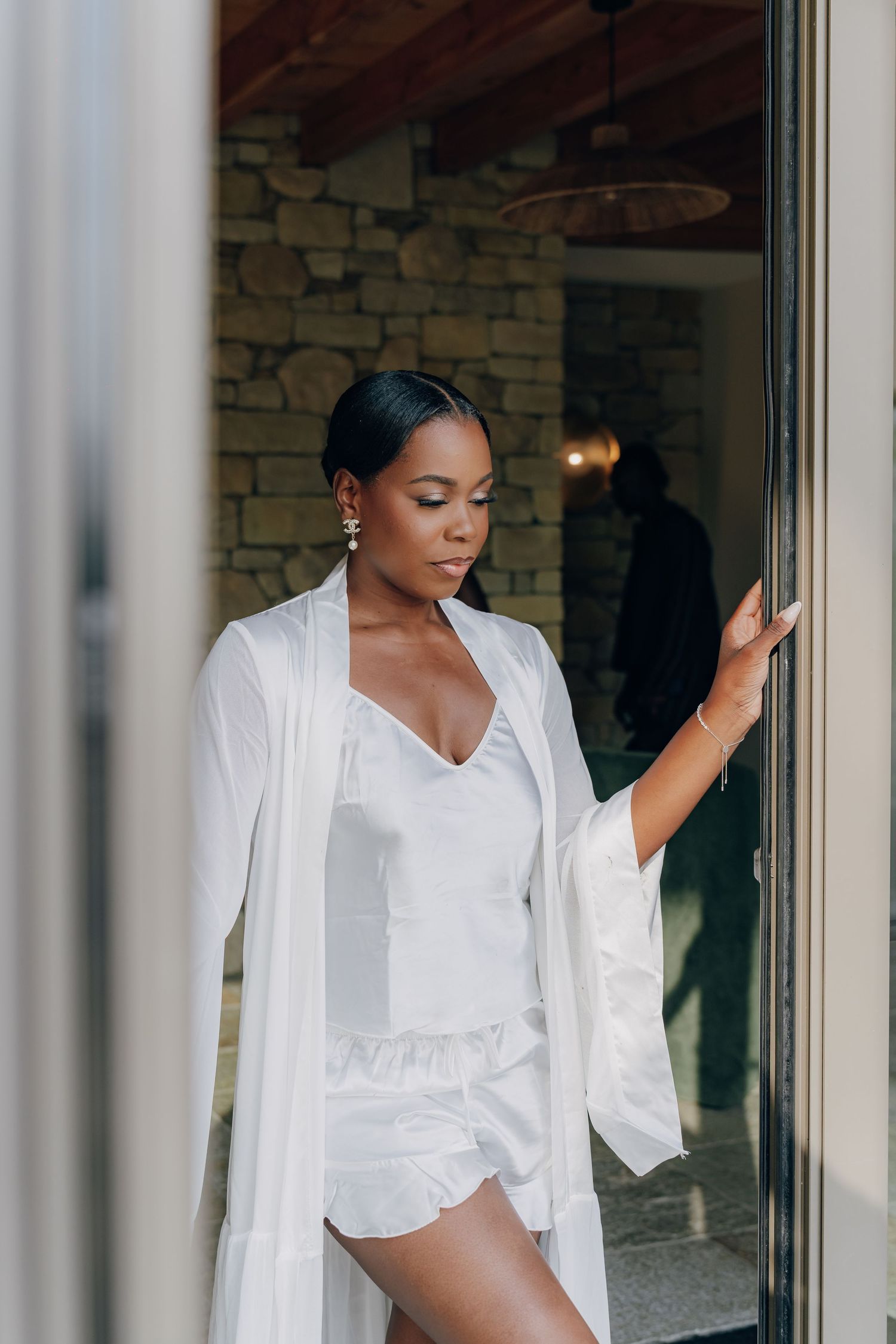 Woman in white robe posing elegantly against a window with natural light streaming in.