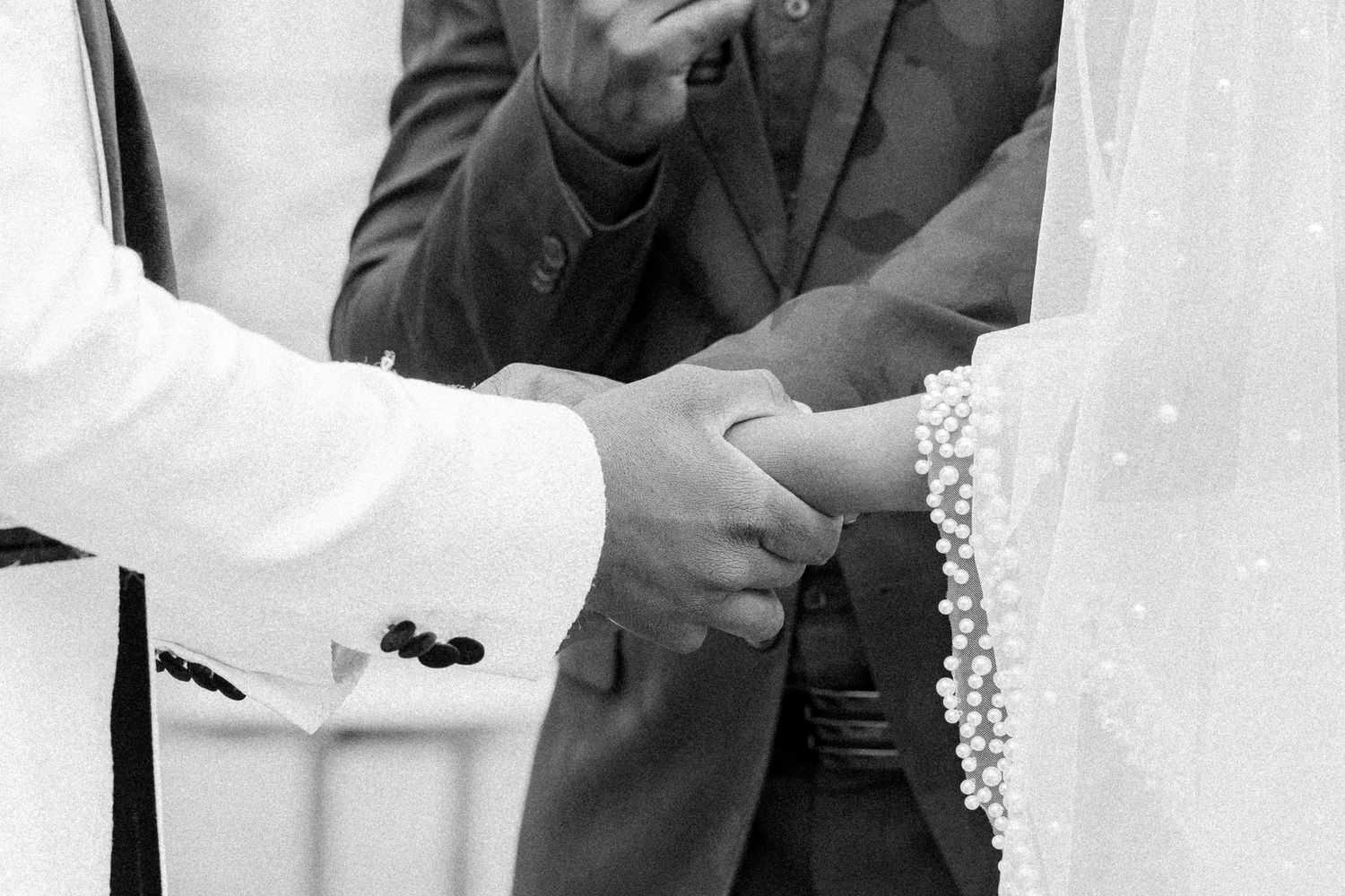 Close-up black and white photo of hands exchanging rings during a wedding ceremony.