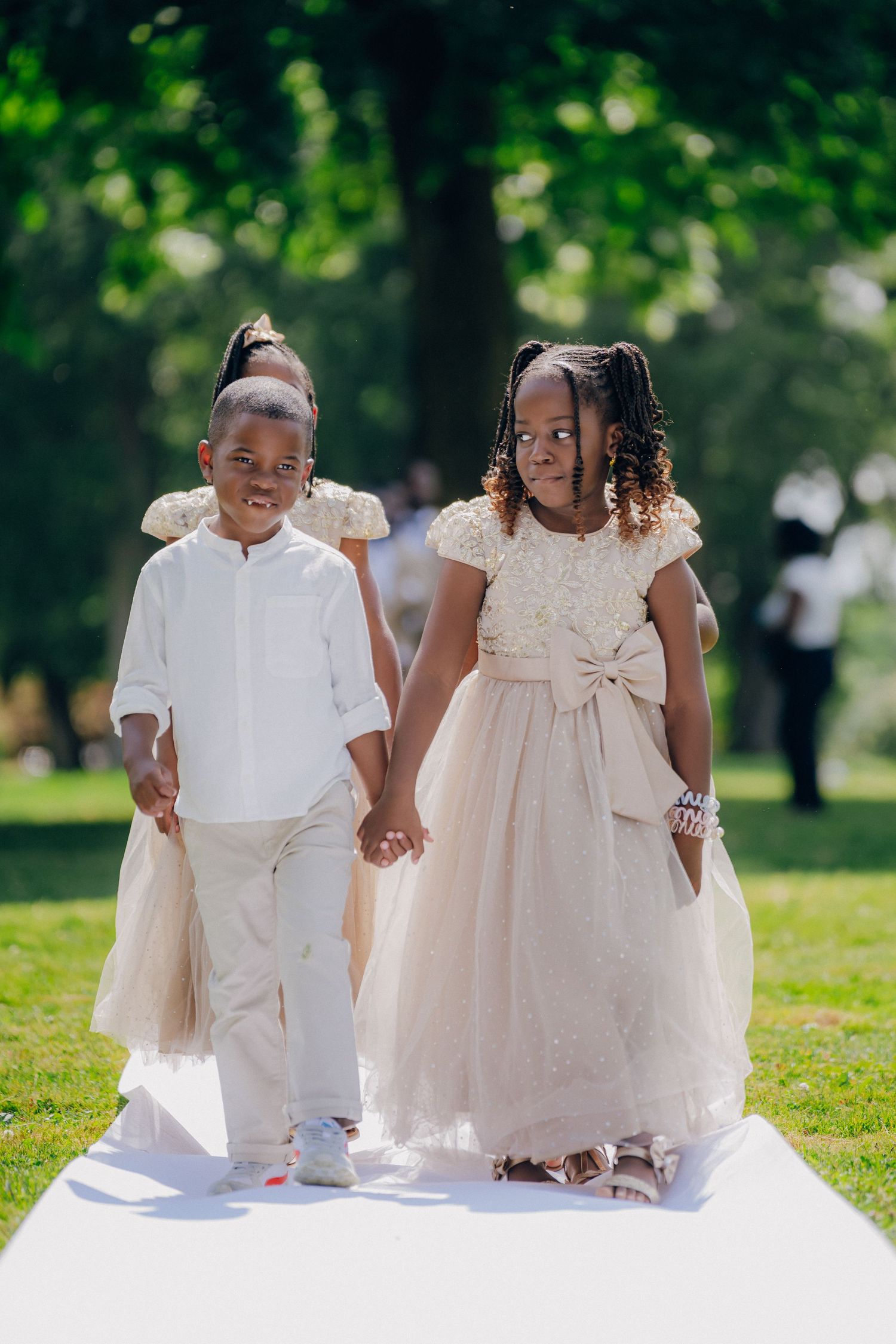 Young children in white and cream formal attire sitting together on a white surface outdoors.