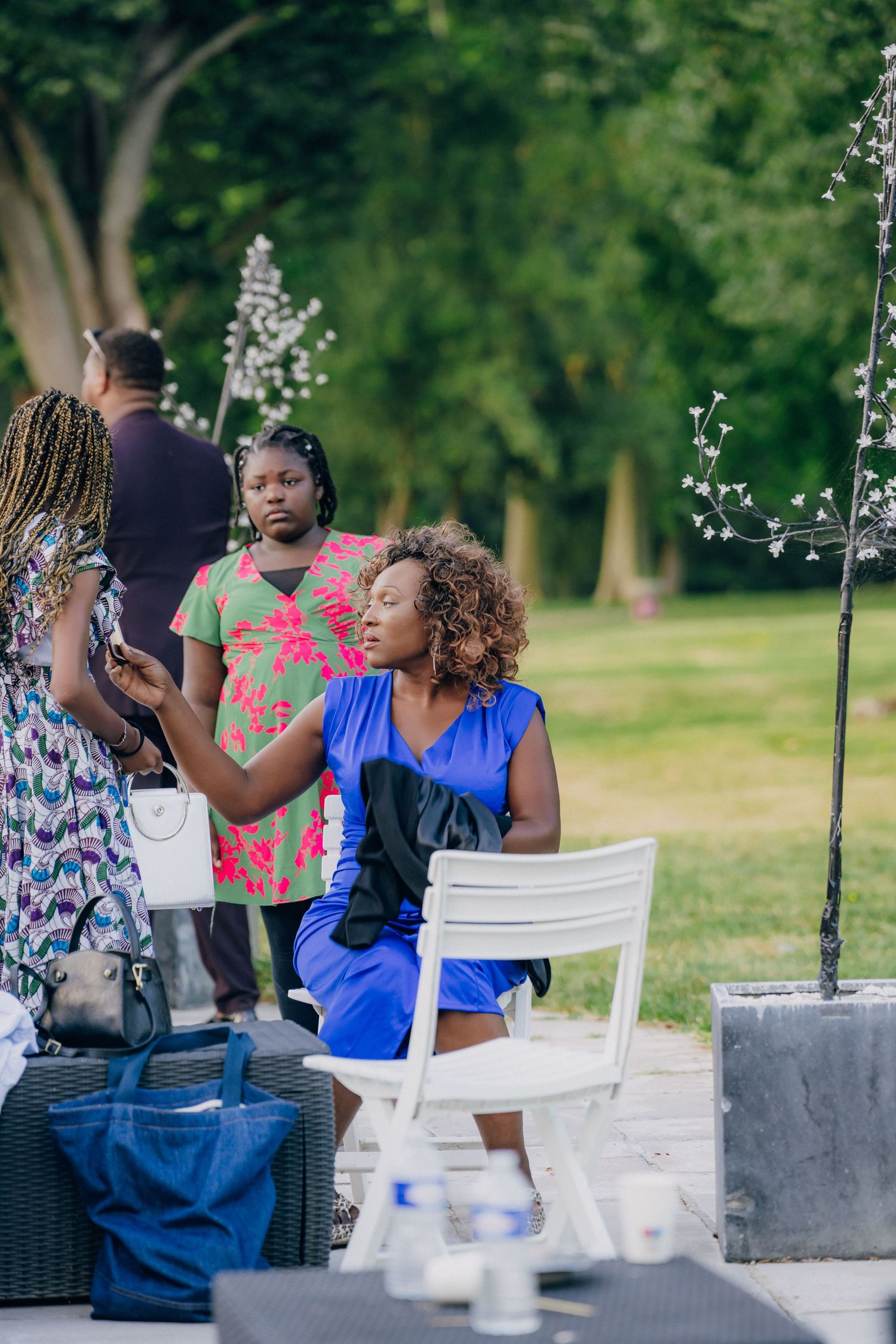 Wedding guests enjoying an outdoor reception with white chairs and decorative lighting in a garden setting.