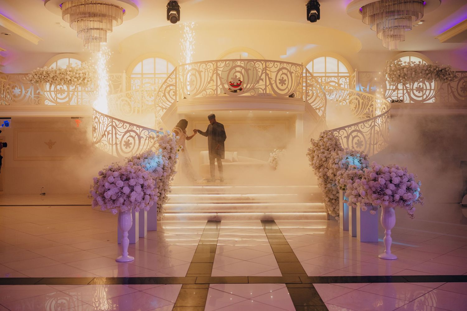 Grand staircase decorated with purple floral arrangements and elegant lighting for a wedding ceremony.