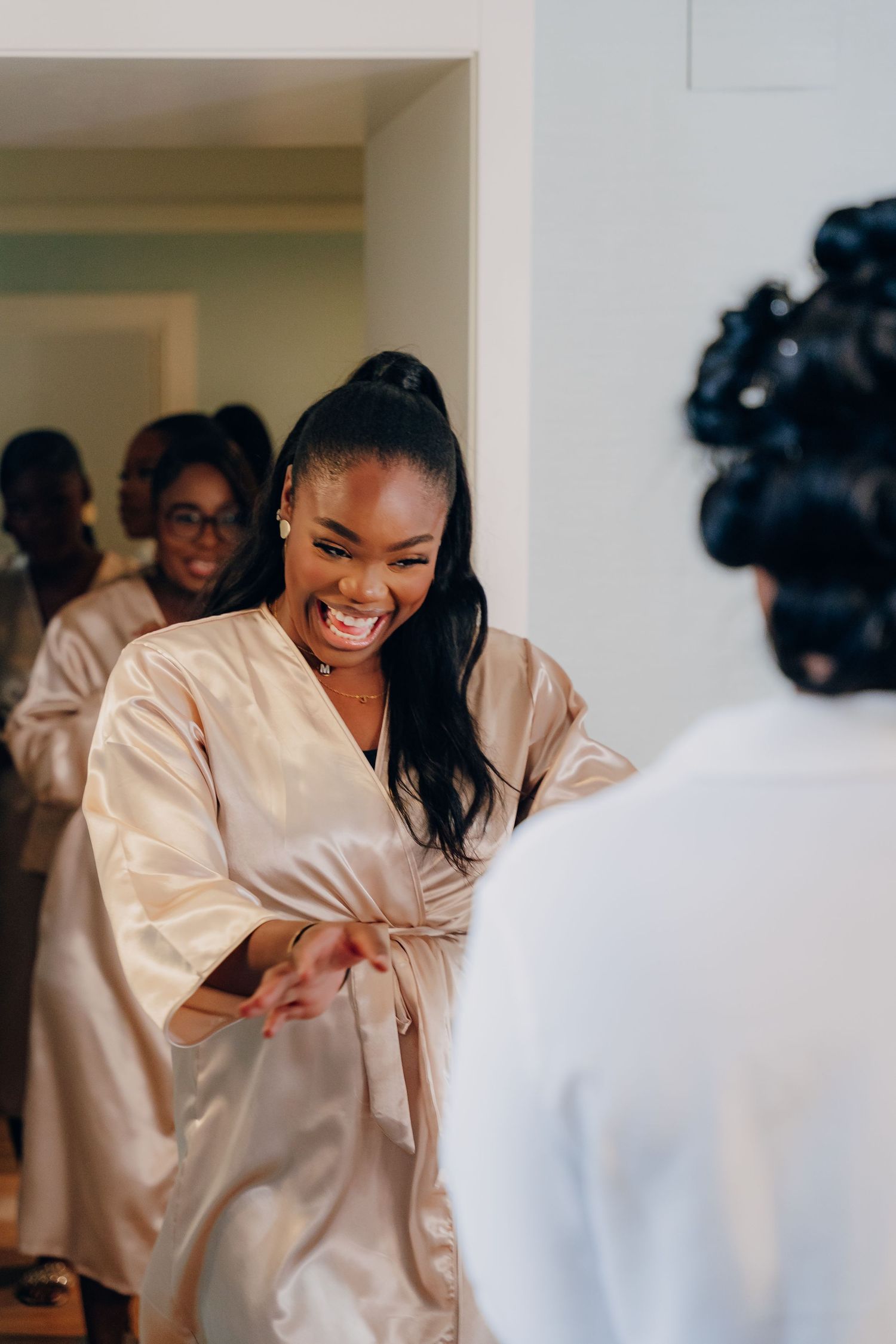 A group of people wearing matching silk robes share joyful laughter during a celebratory getting-ready moment.
