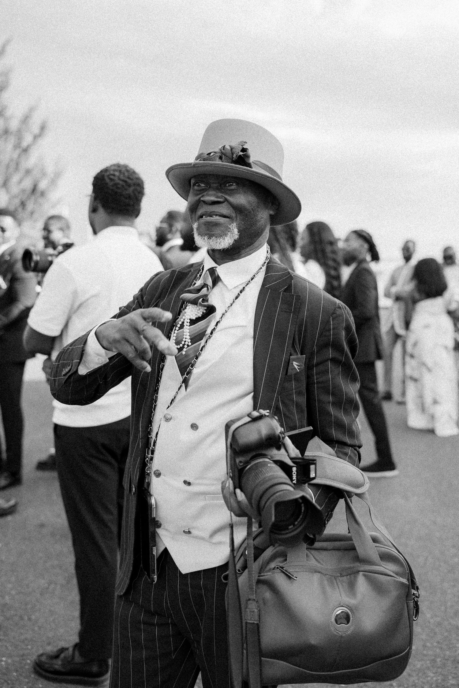Black and white photo of guests in formal attire enjoying themselves at an outdoor celebration.