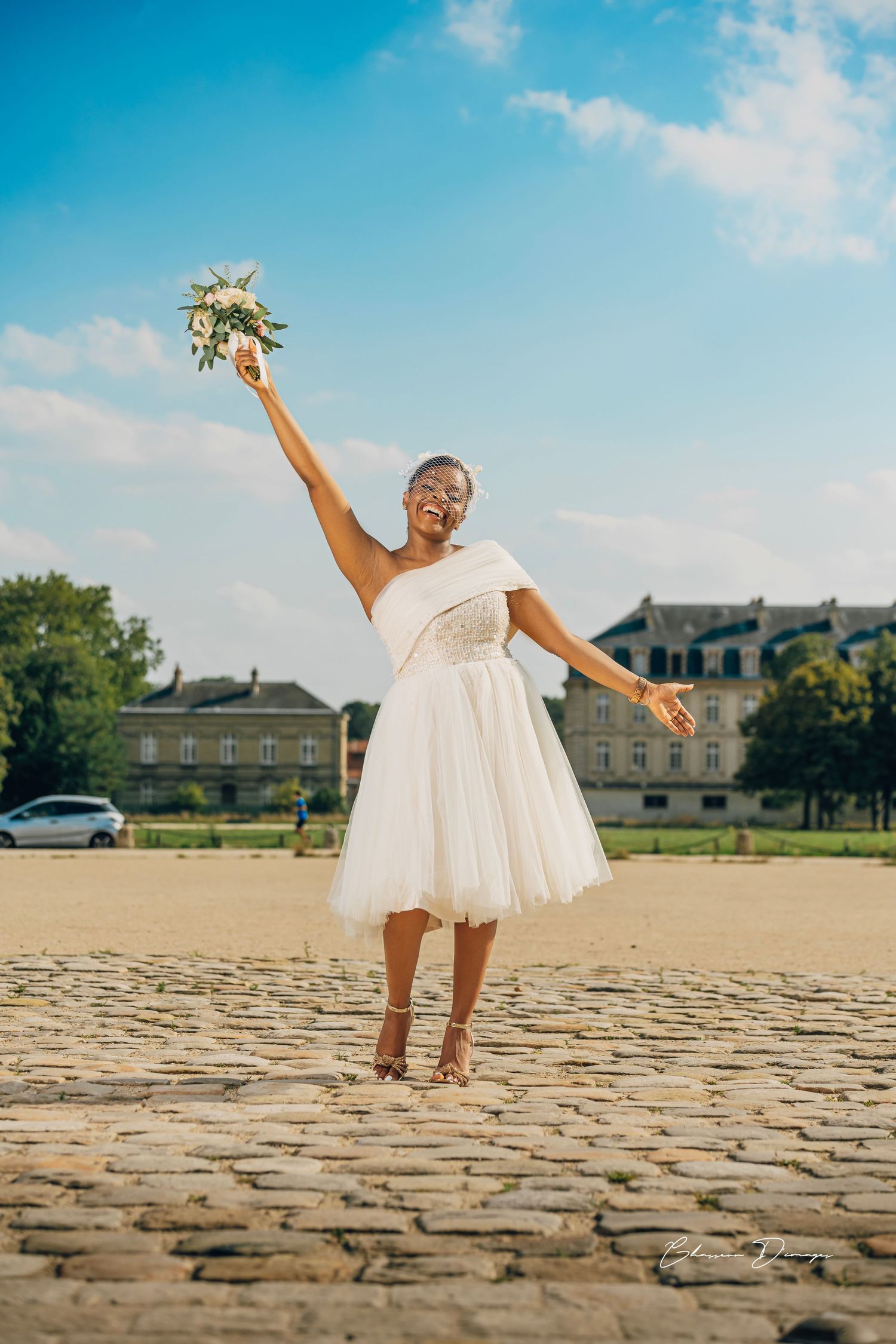 Joyful moment in white dress holding bouquet aloft on cobblestone square.