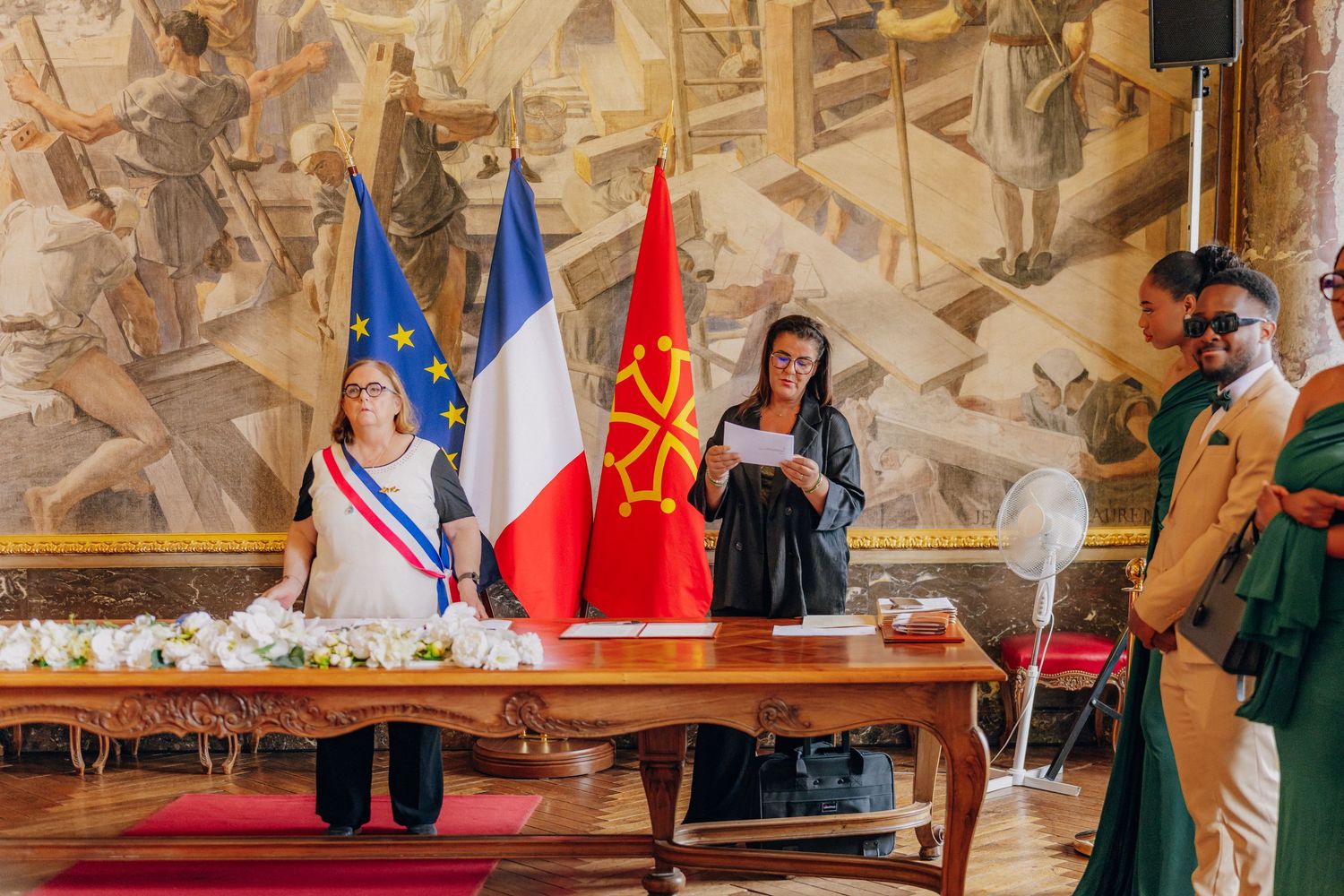 Diplomatic ceremony taking place in an ornate palace room with flags and decorative murals on the walls.