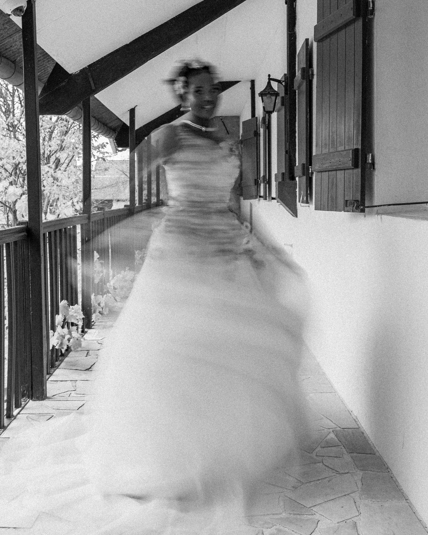 A blurred black and white motion photo shows someone in a white dress moving through a covered walkway.