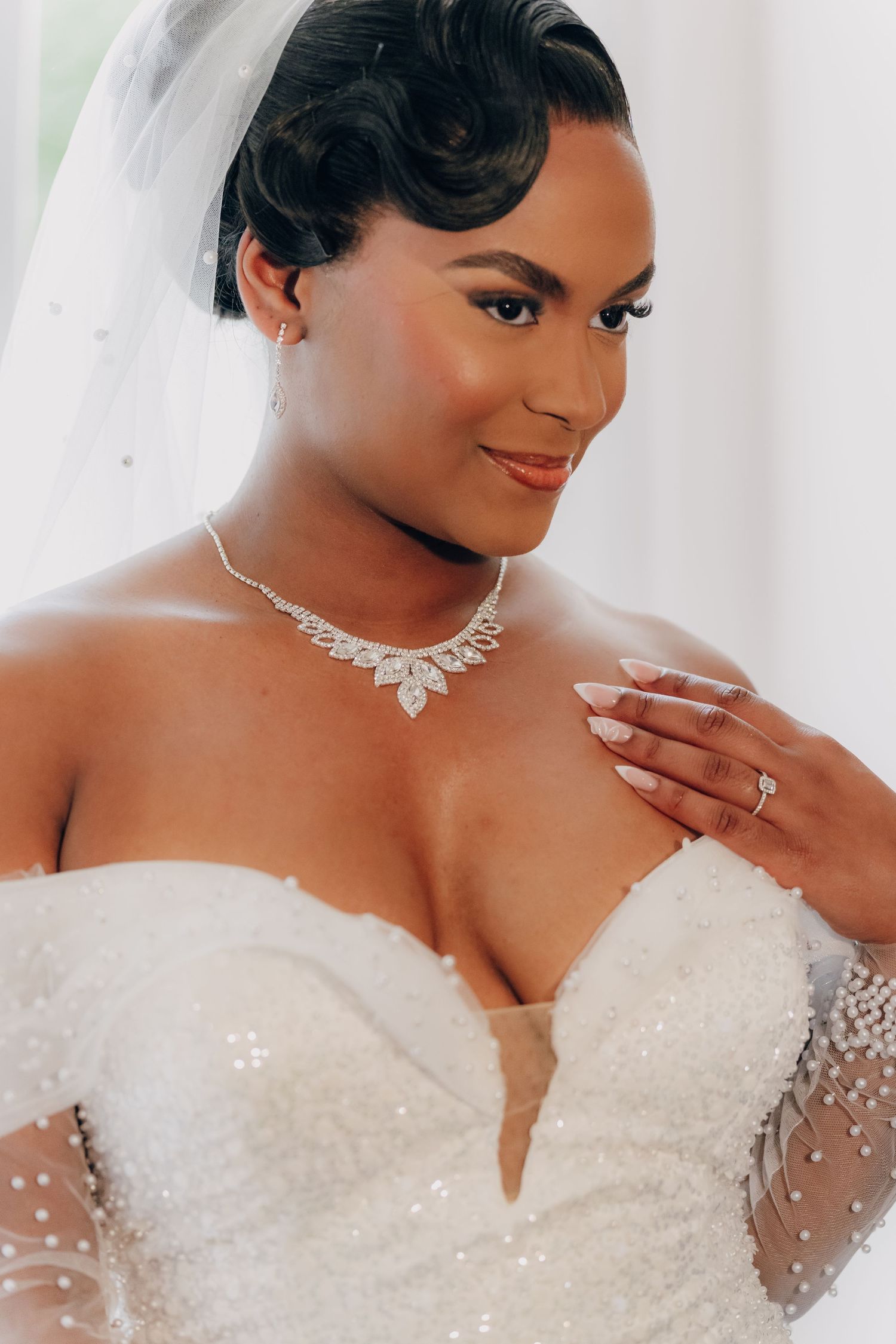 Close-up details of a bride wearing an elegant white beaded wedding gown with sheer sleeves and sparkling jewelry.
