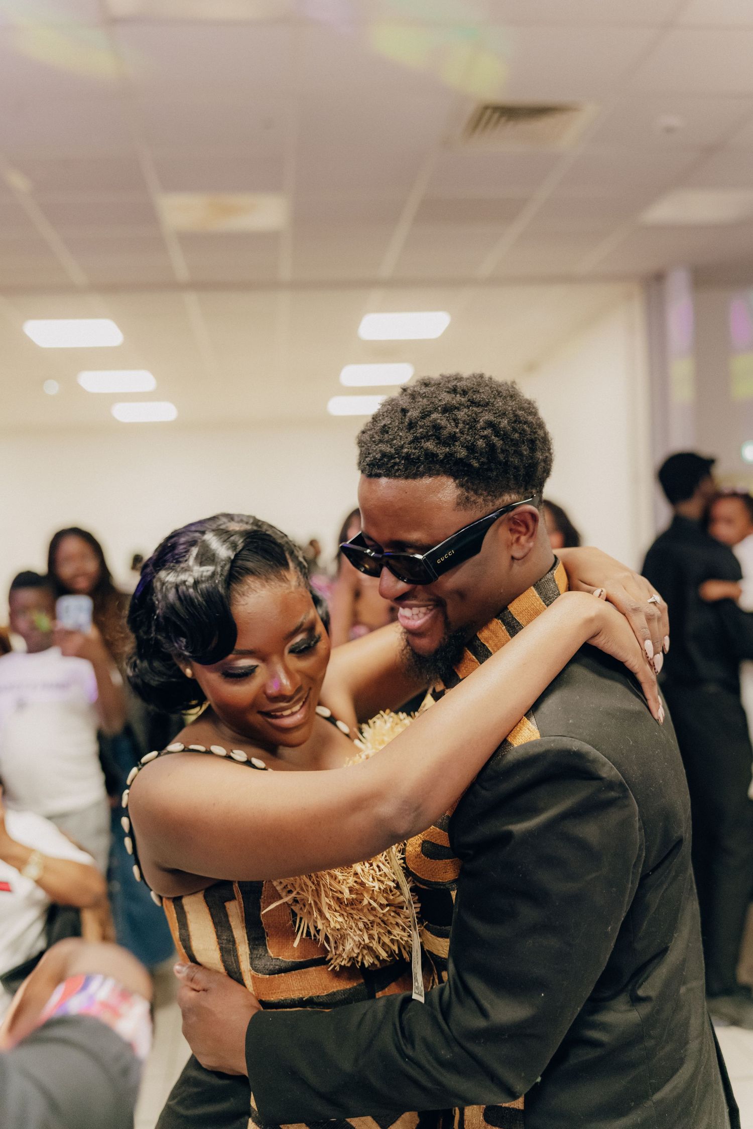 A couple embraces and laughs together at a celebration, one in gold attire and the other in dark clothing.