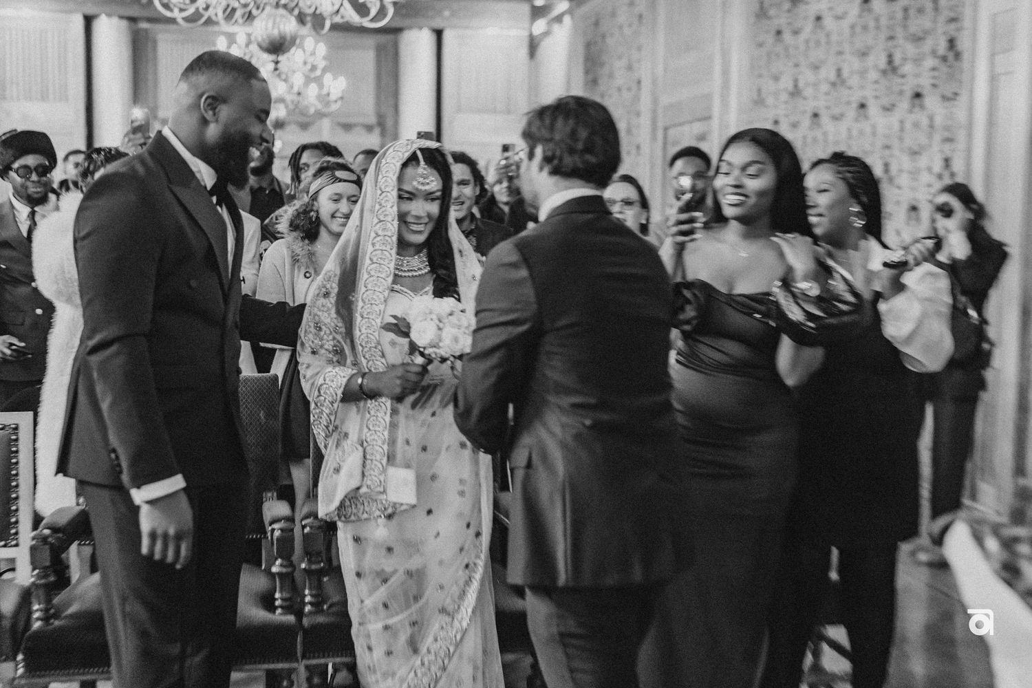 Black and white photo of a wedding ceremony with guests celebrating in an ornate indoor venue.