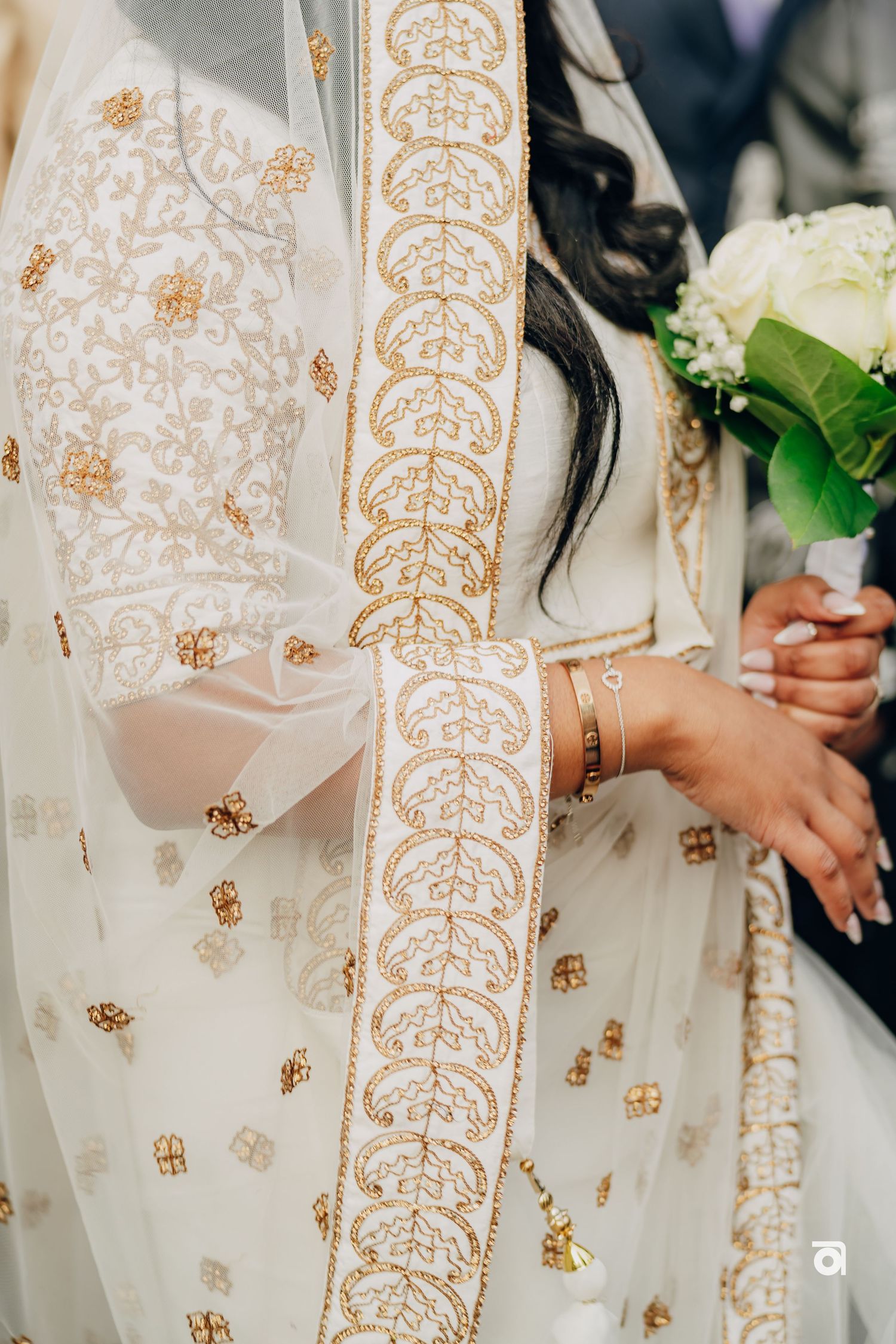 Detail shot of ornate gold embroidered wedding dress with white flowers.