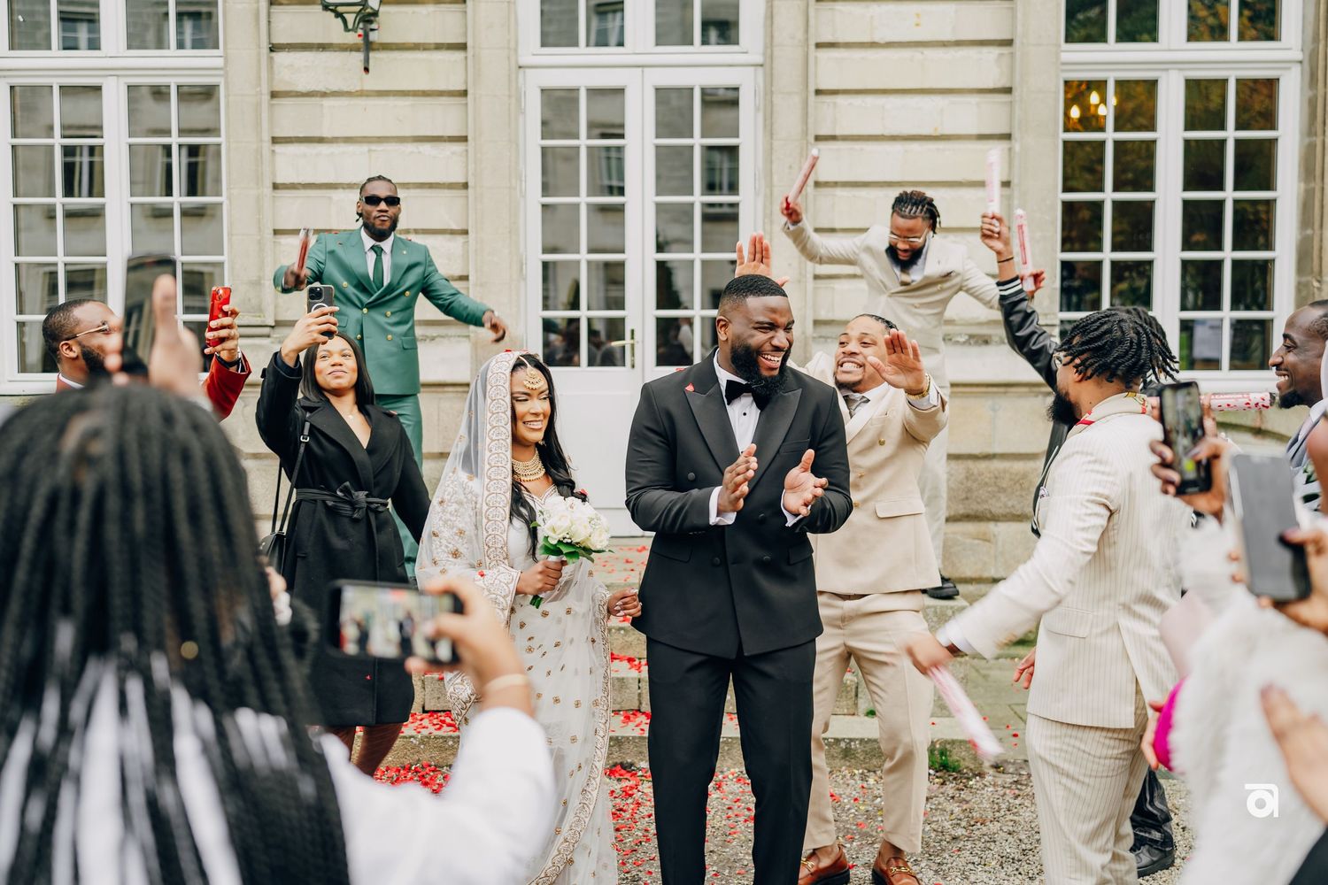 Joyful wedding celebration with guests in light-colored attire outside historic building.
