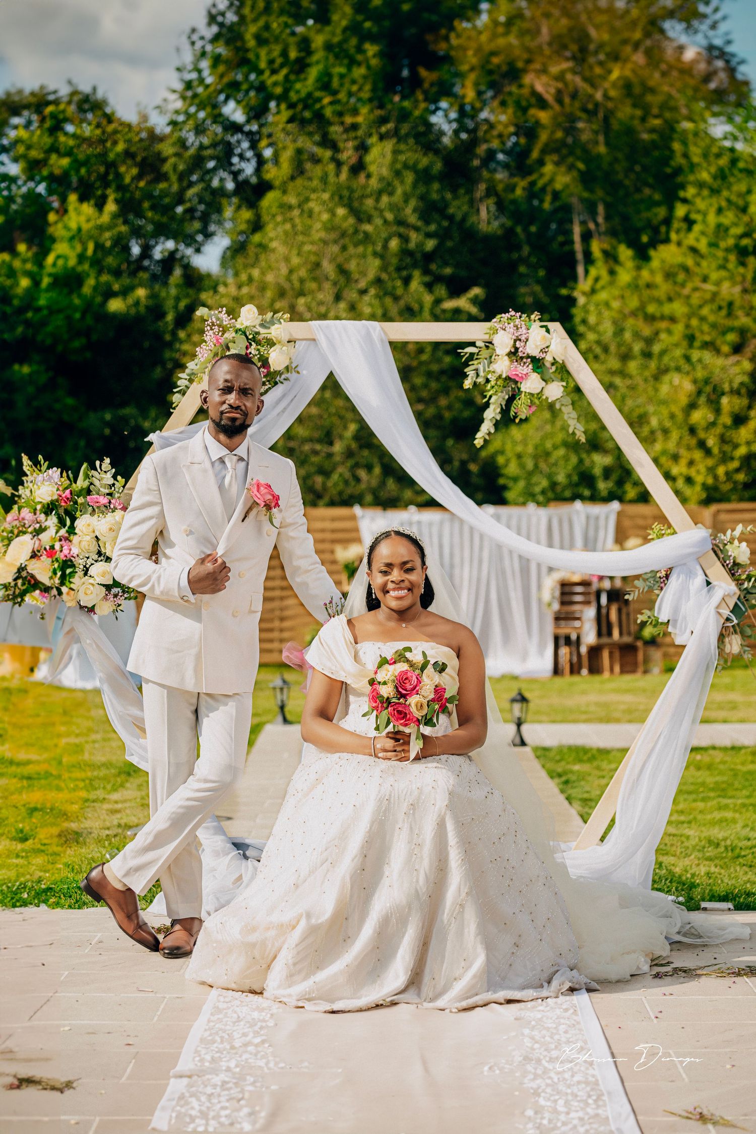 Wedding couple poses by floral arch during outdoor garden ceremony.