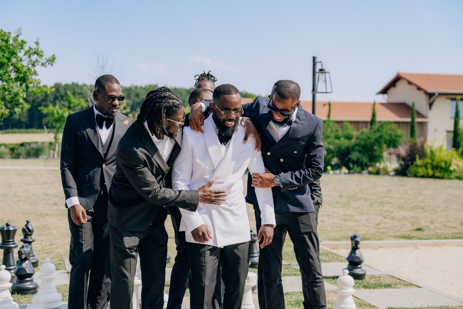 A group in formal attire shares a lighthearted moment outdoors during what appears to be a wedding celebration.