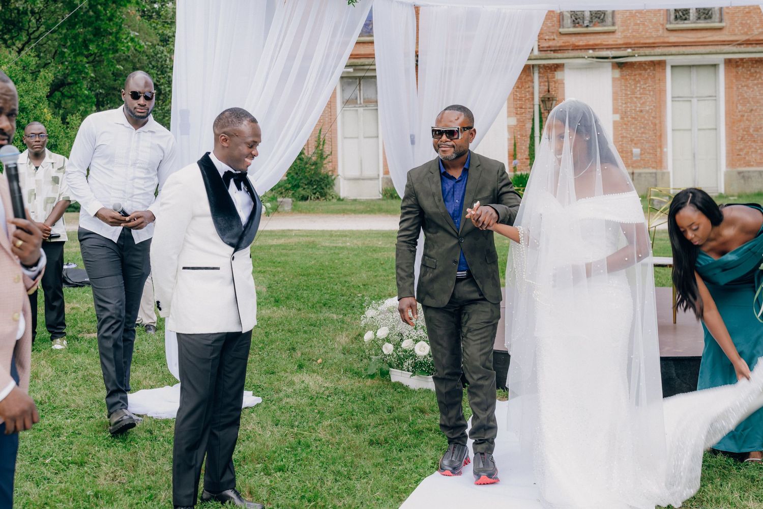 Outdoor wedding celebration with white draped archway and guests gathered on the lawn.