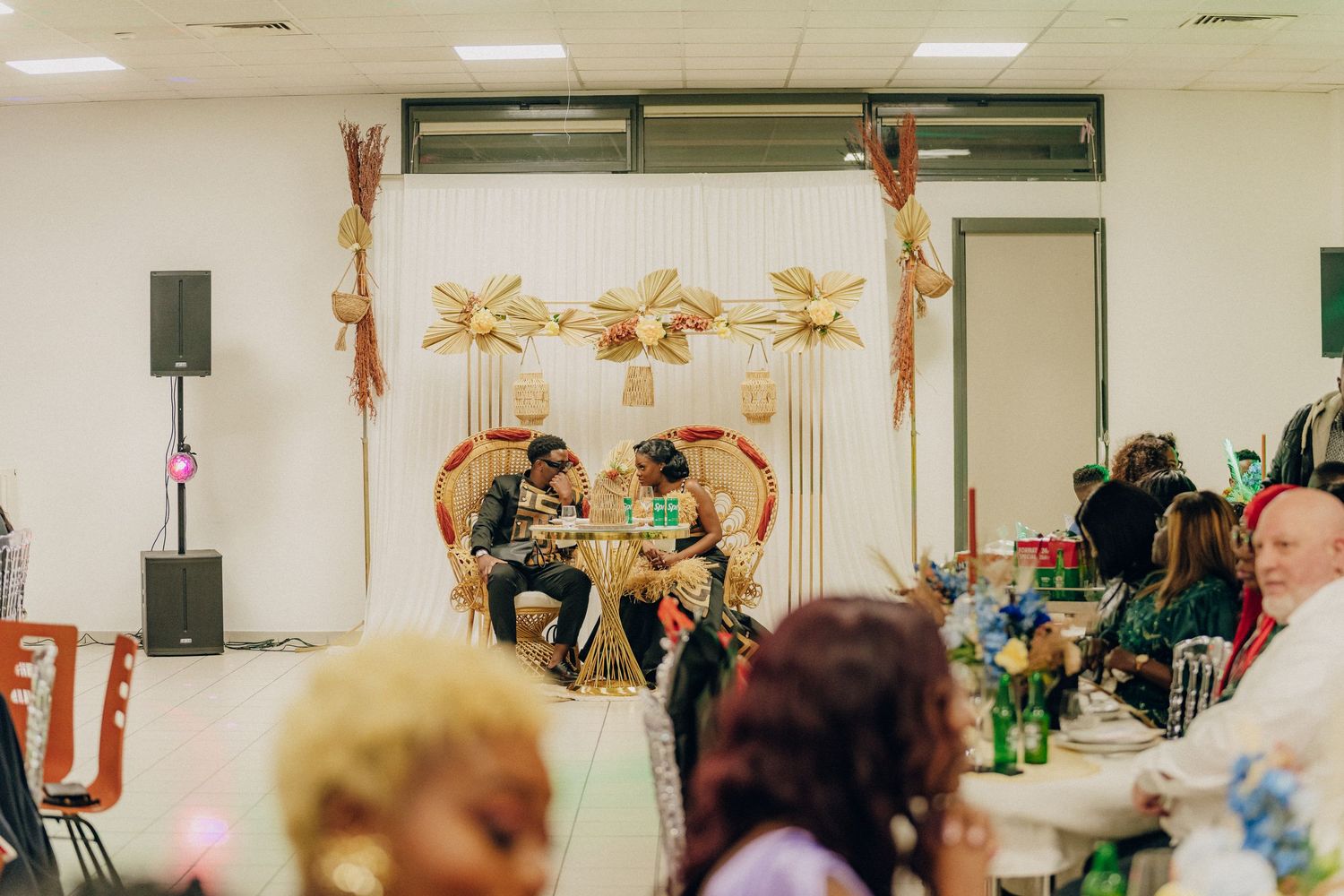 Wedding reception scene with gold decorations and guests seated at tables in a community hall.