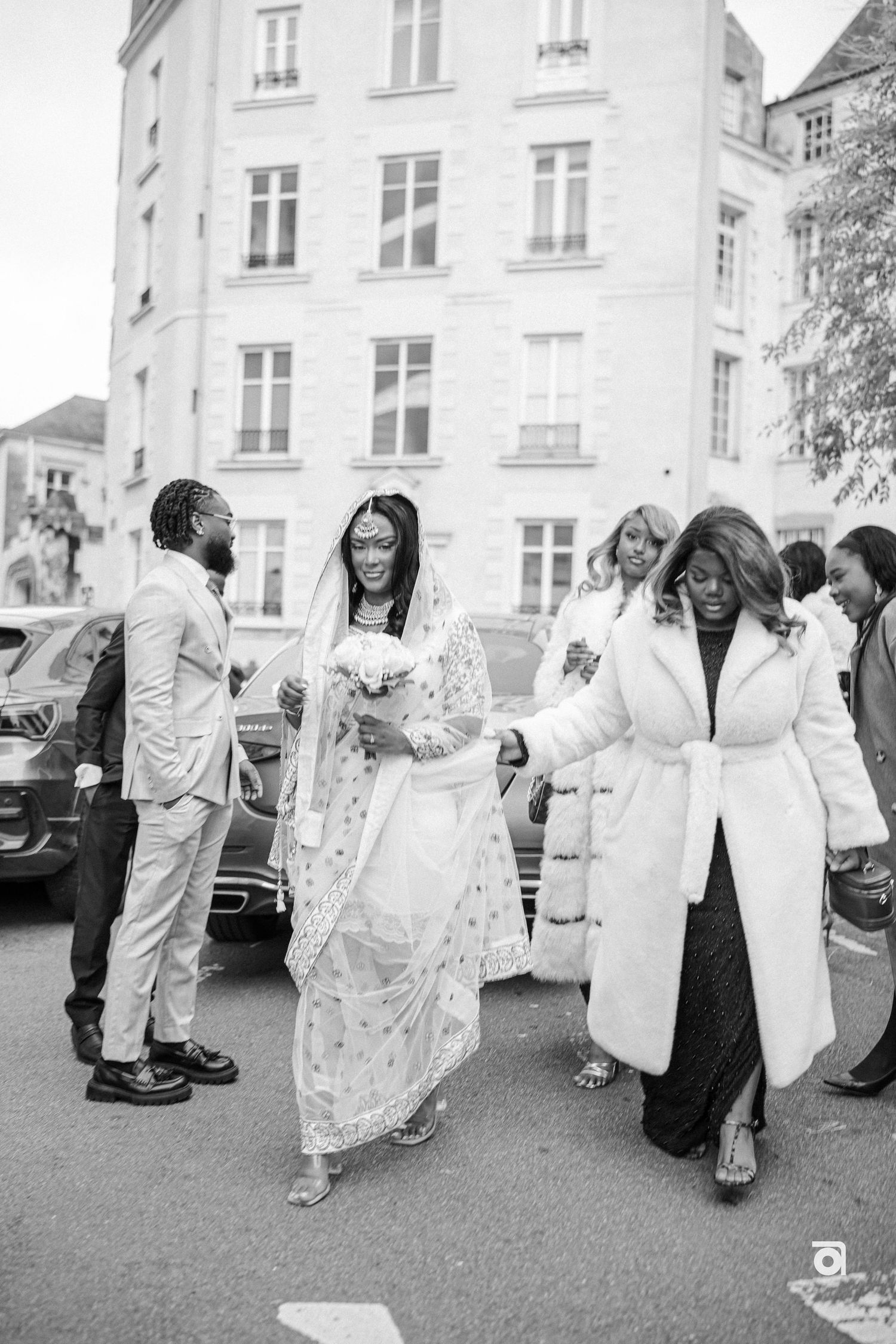 A wedding celebration outside a classic European building with a bride in white lace dress surrounded by guests.