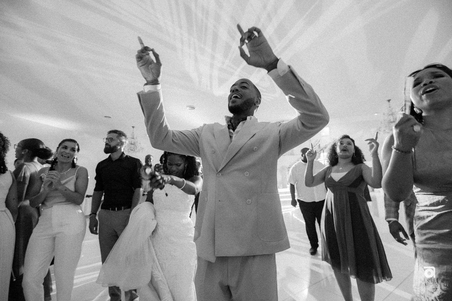 A joyful celebration in black and white as people dance at what appears to be a wedding reception or party.