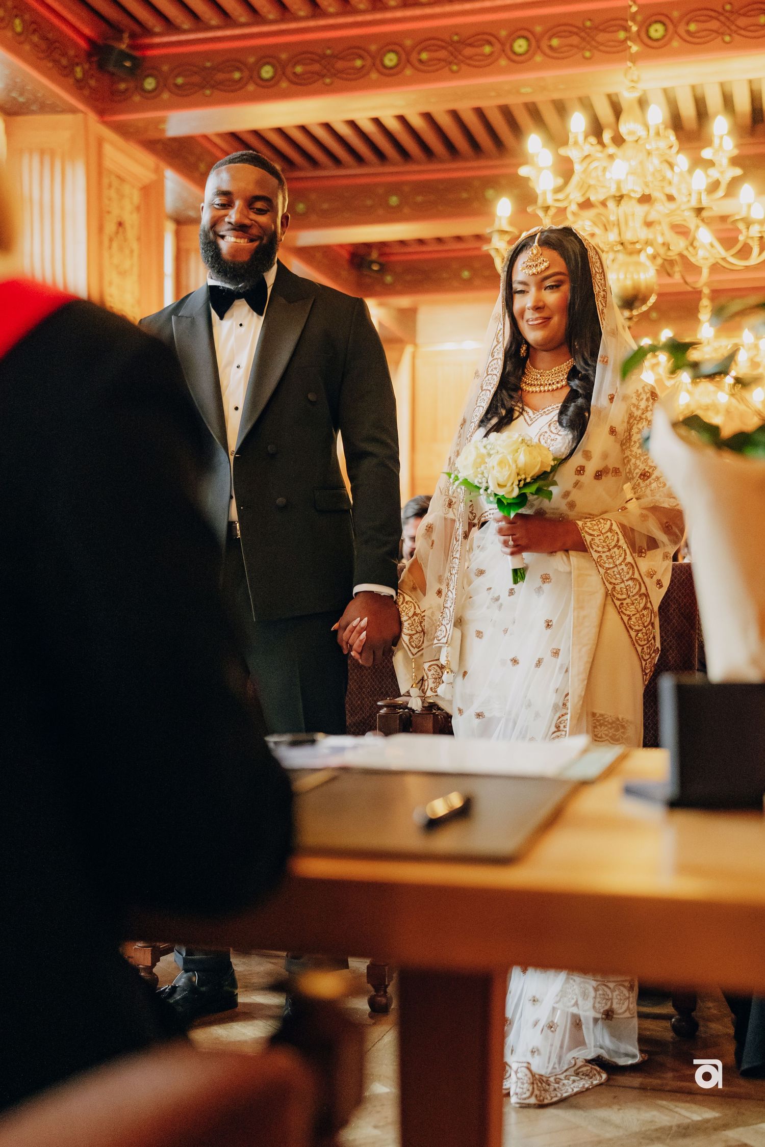 A couple shares a joyful moment during their wedding ceremony in an elegant room with a chandelier.