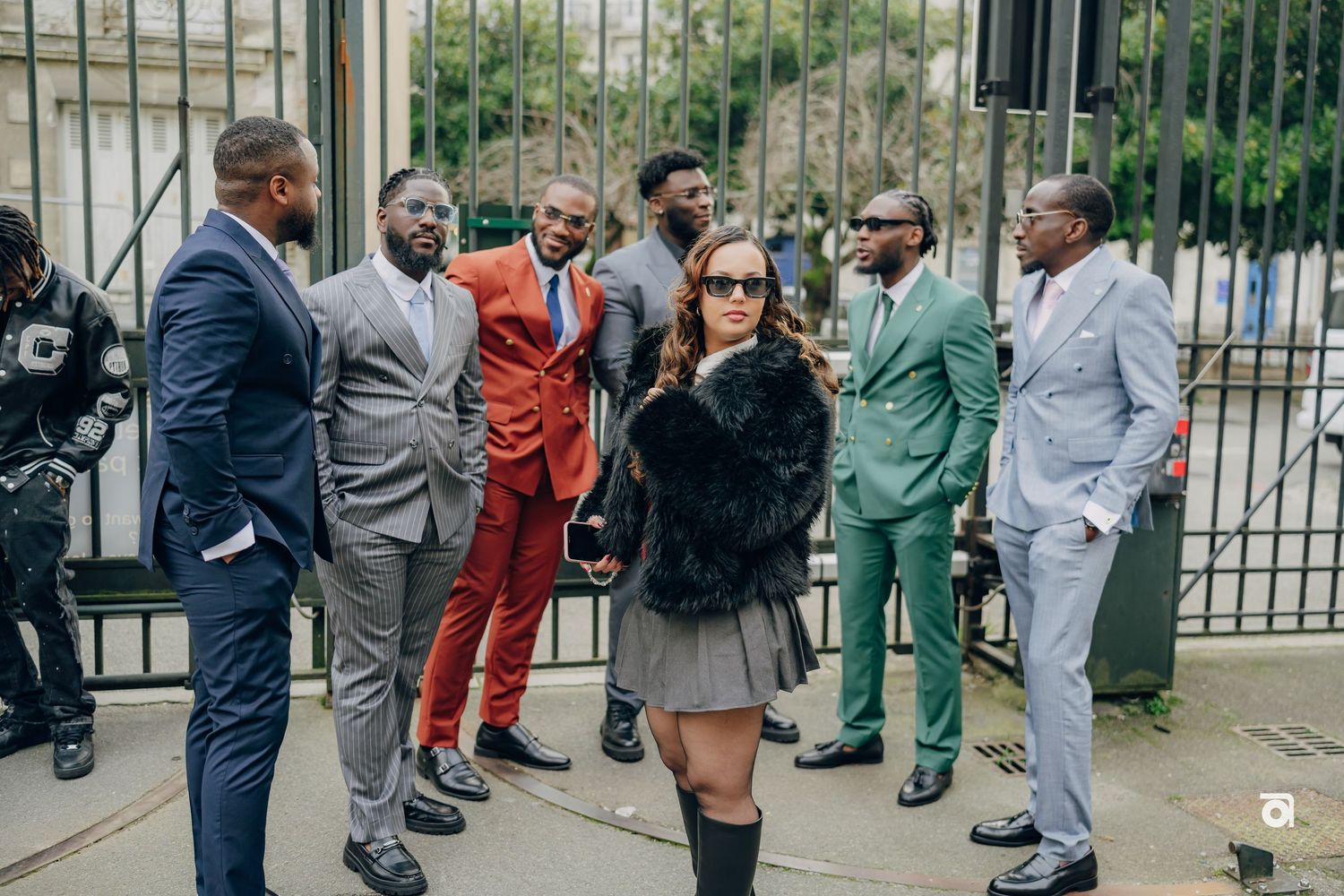 A group of well-dressed people in colorful suits pose together in front of an iron gate outdoors.