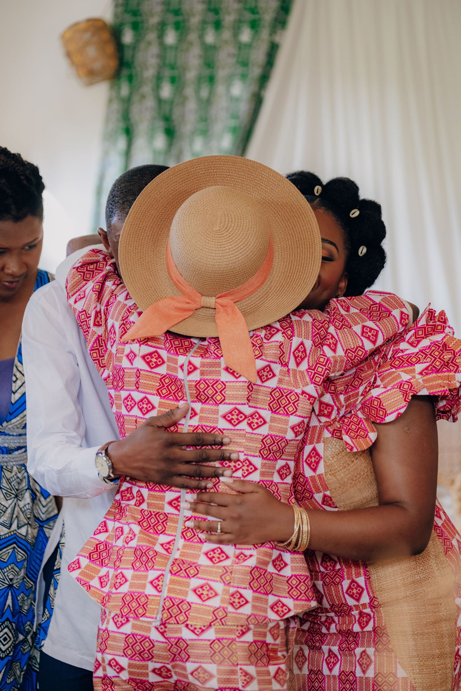 A tender moment at a celebration with people wearing colorful floral prints and a straw hat.