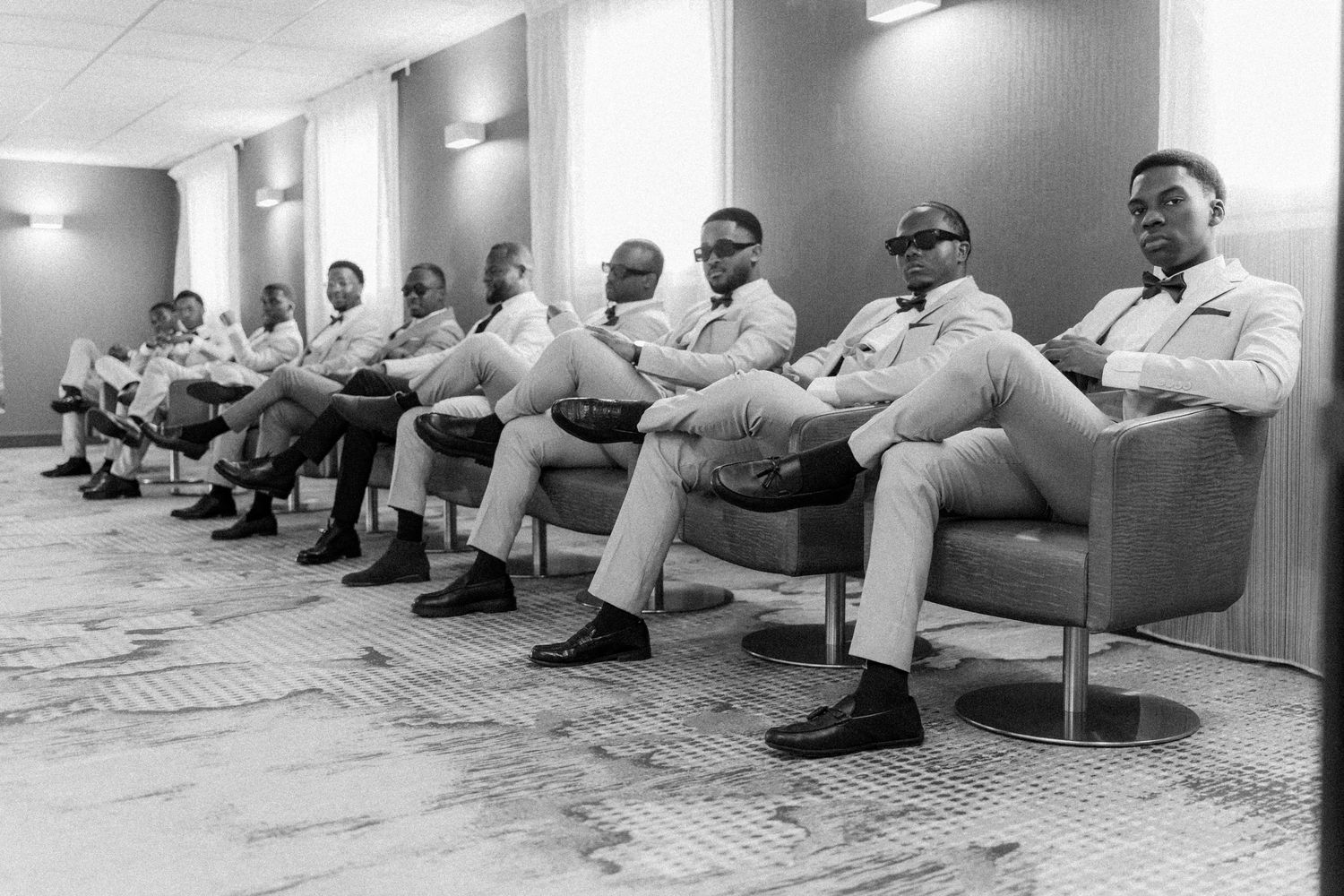 People sitting in white chairs along a wall in what appears to be a waiting room.