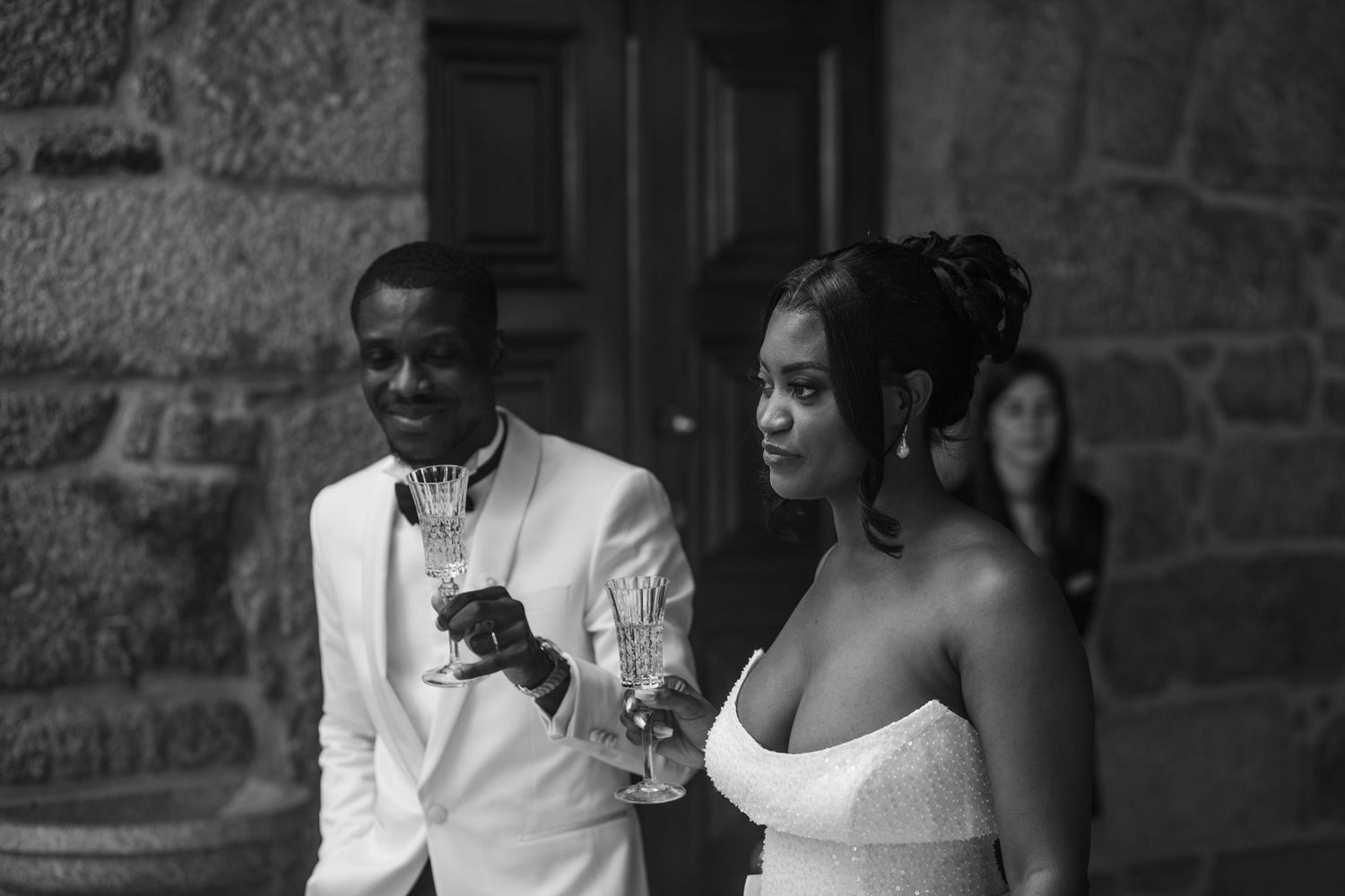 Black and white portrait of couple in formal attire against stone wall.