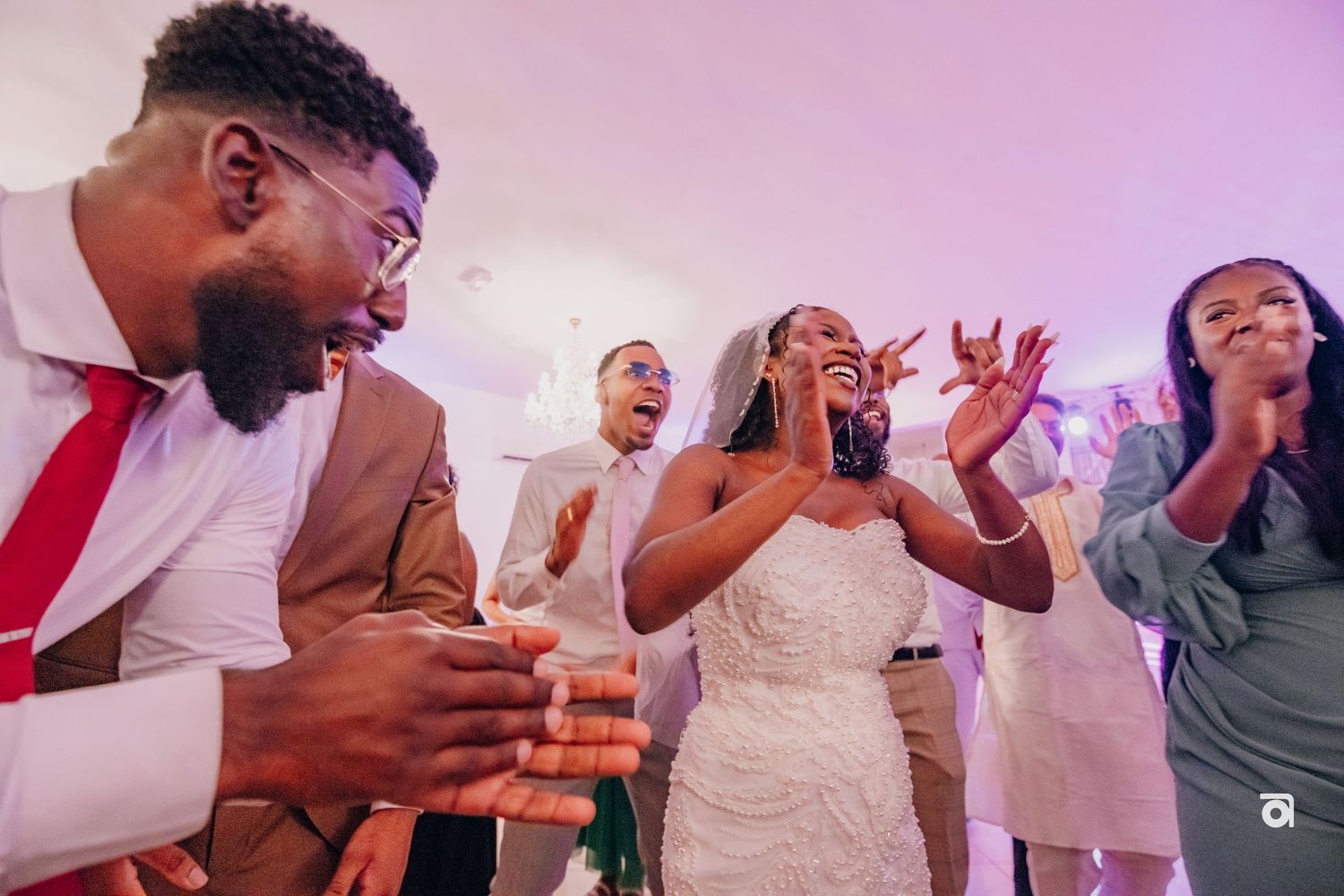 A group of wedding guests react with joy and excitement while dancing and celebrating at a reception party.