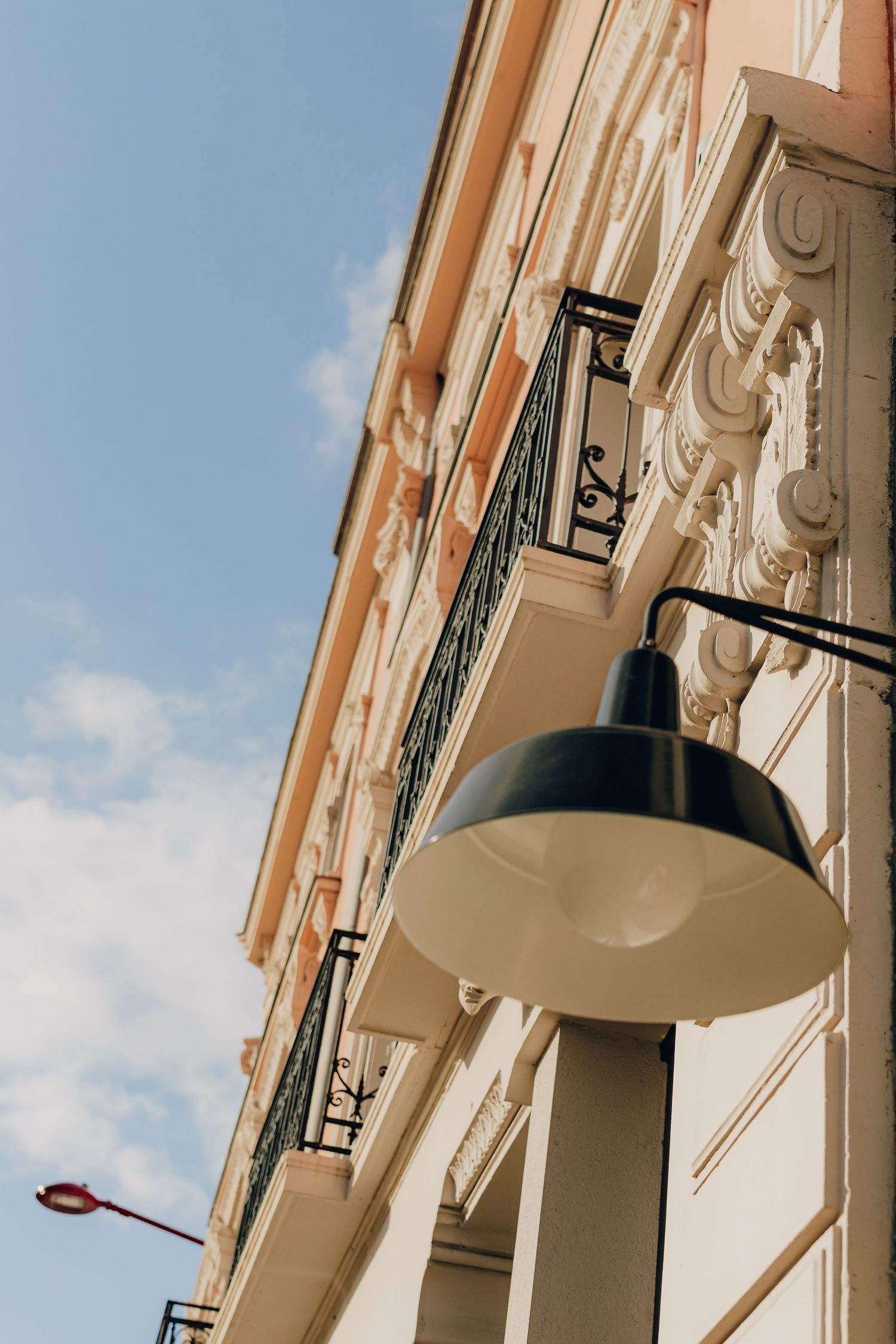 Architectural detail of beige building facade with ornate moldings and black industrial lamp against blue sky.