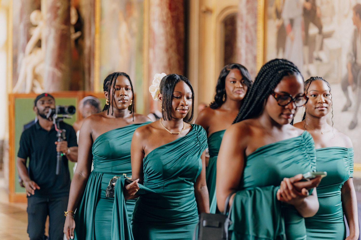 Wedding party members in teal dresses celebrate joyfully in an elegant hallway.