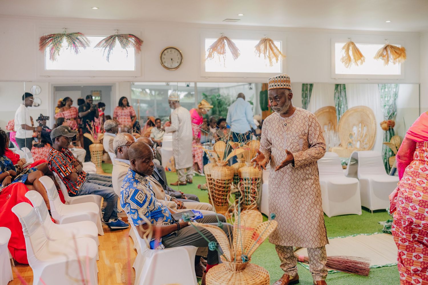 A panoramic view of a wedding celebration showing guests in colorful African prints gathered in a white room.