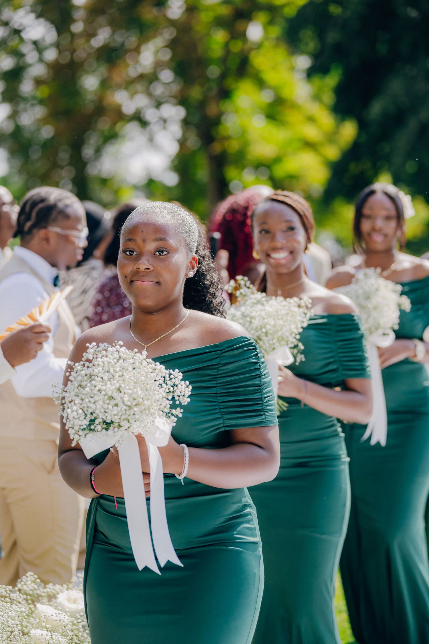 Bridesmaids in elegant emerald green dresses holding white baby's breath bouquets at an outdoor wedding.