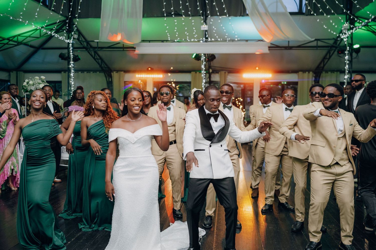 Wedding party dancing and celebrating on dance floor with colorful green and orange lighting effects.