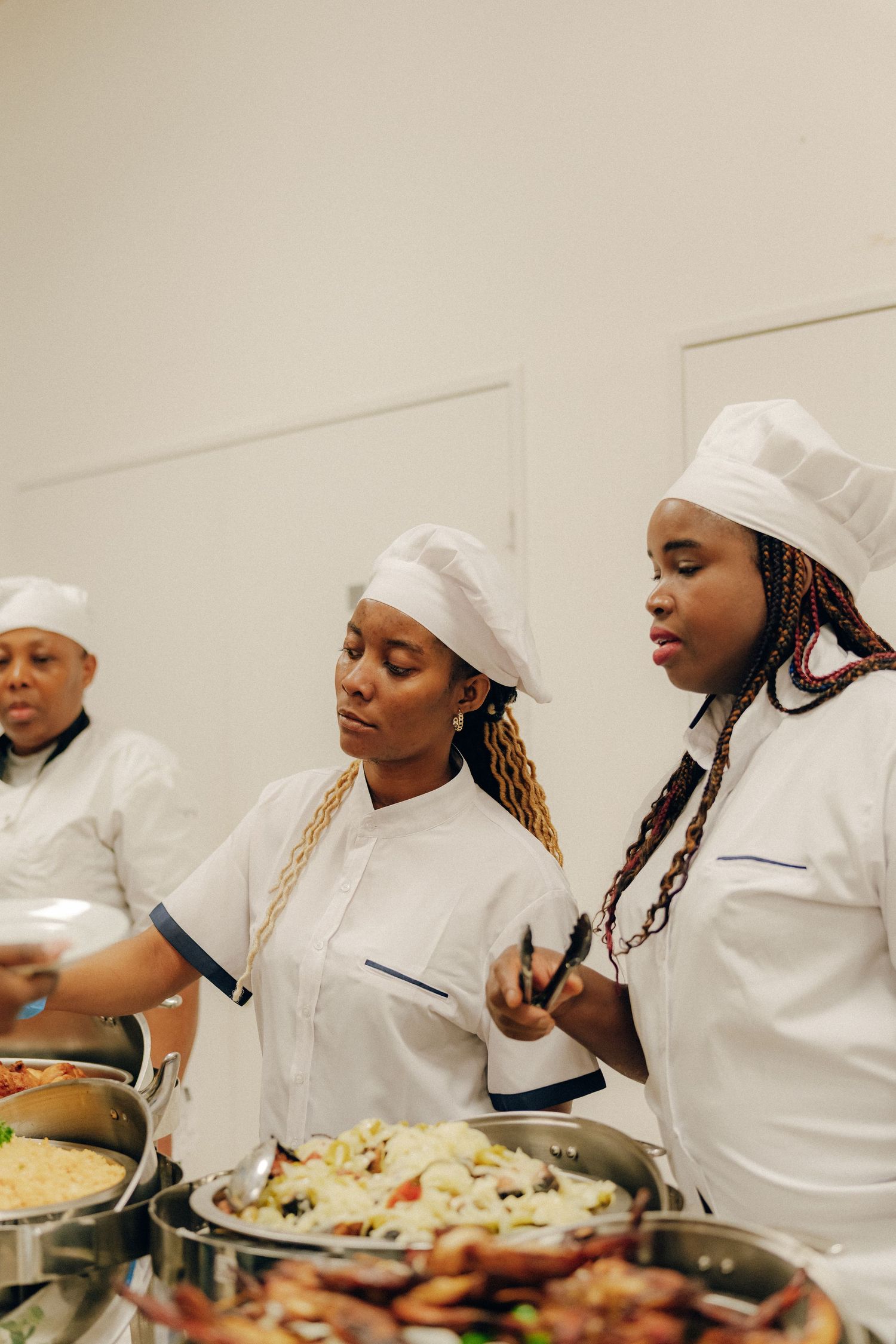Culinary professionals in white chef coats and hats prepare various dishes at a catering station.