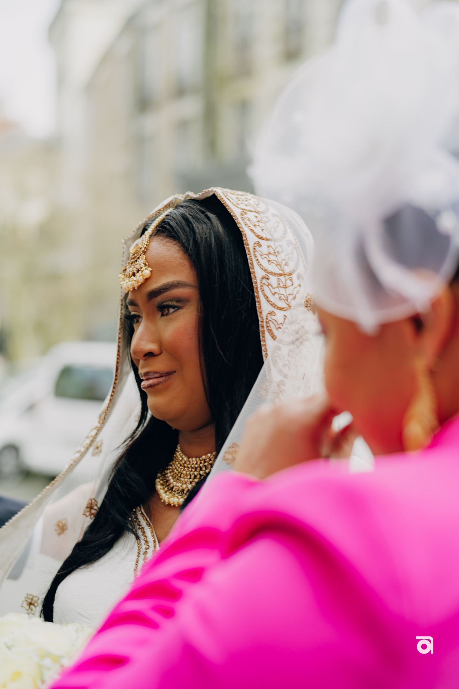 A bride wearing an ornate white and gold veil with traditional Indian wedding jewelry and long dark hair.