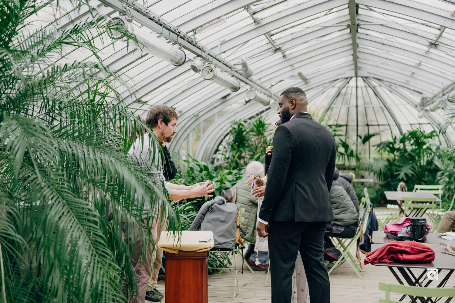 Musicians performing at a wedding ceremony inside a light-filled greenhouse surrounded by tropical plants.