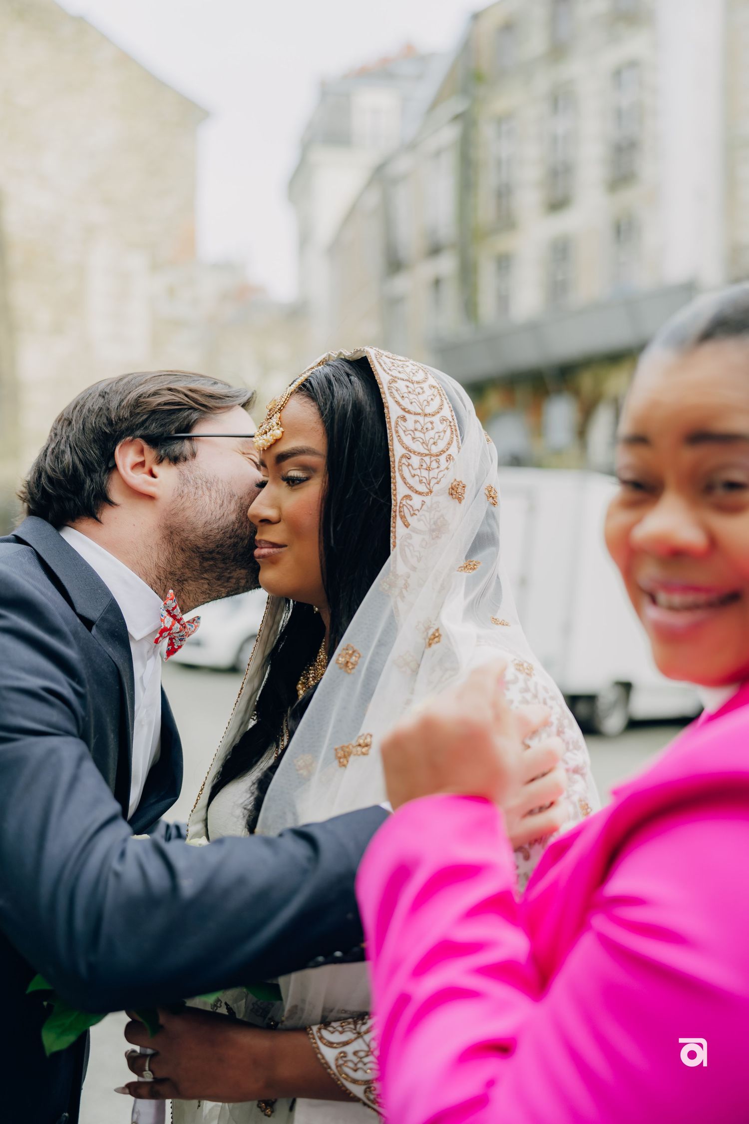 A tender moment shared between a couple outside with the bride wearing an elegant white veil and another person in pink.
