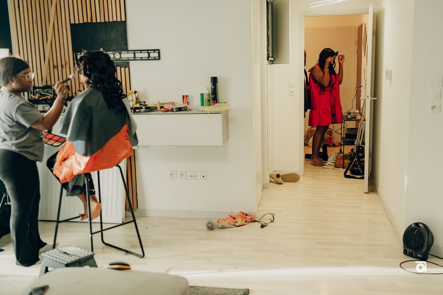 People sitting at kitchen counter in modern apartment with wooden floors and open doorway to another room.
