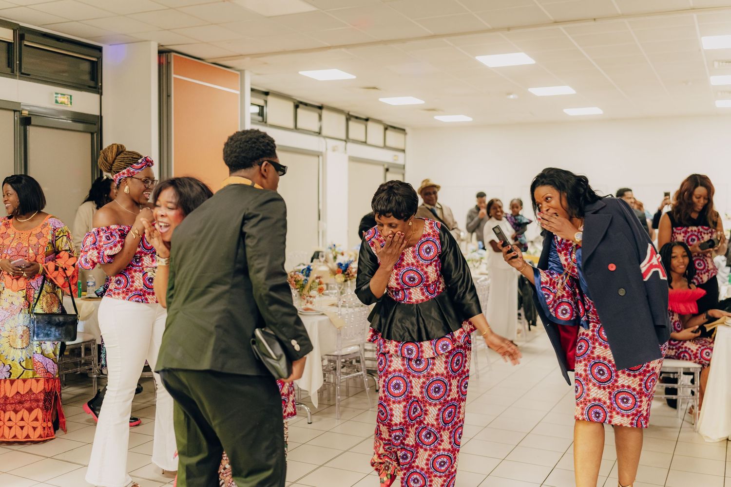 People dancing together in a bright indoor space wearing vibrant pink and red patterned traditional clothing.