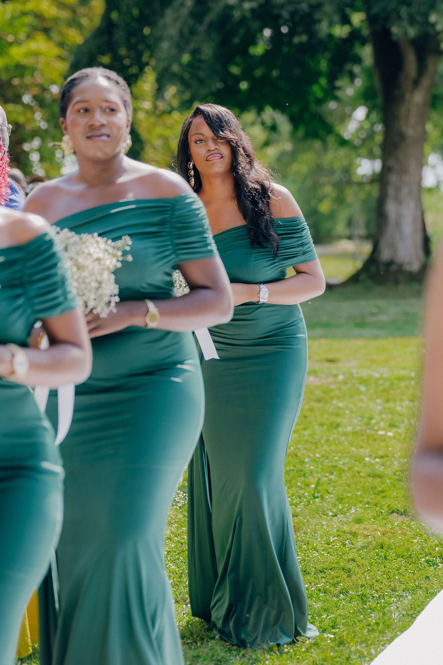 Bridesmaids in elegant green off-shoulder dresses stand together during outdoor wedding ceremony.