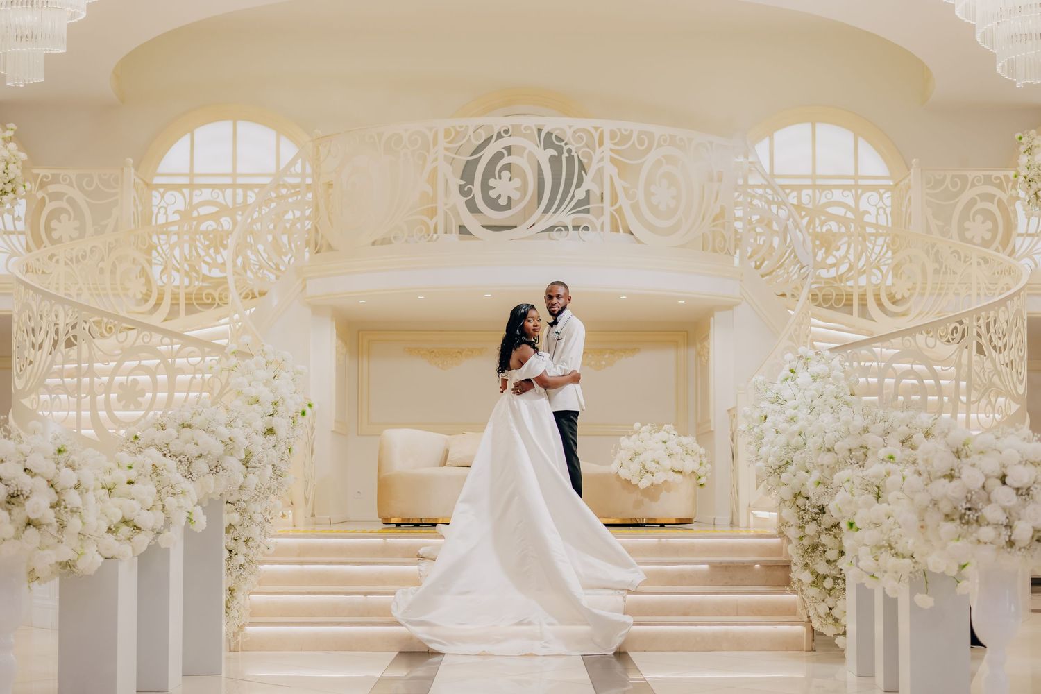 A romantic wedding photoshoot in an elegant cream-colored ballroom with ornate architectural details and floral decor.