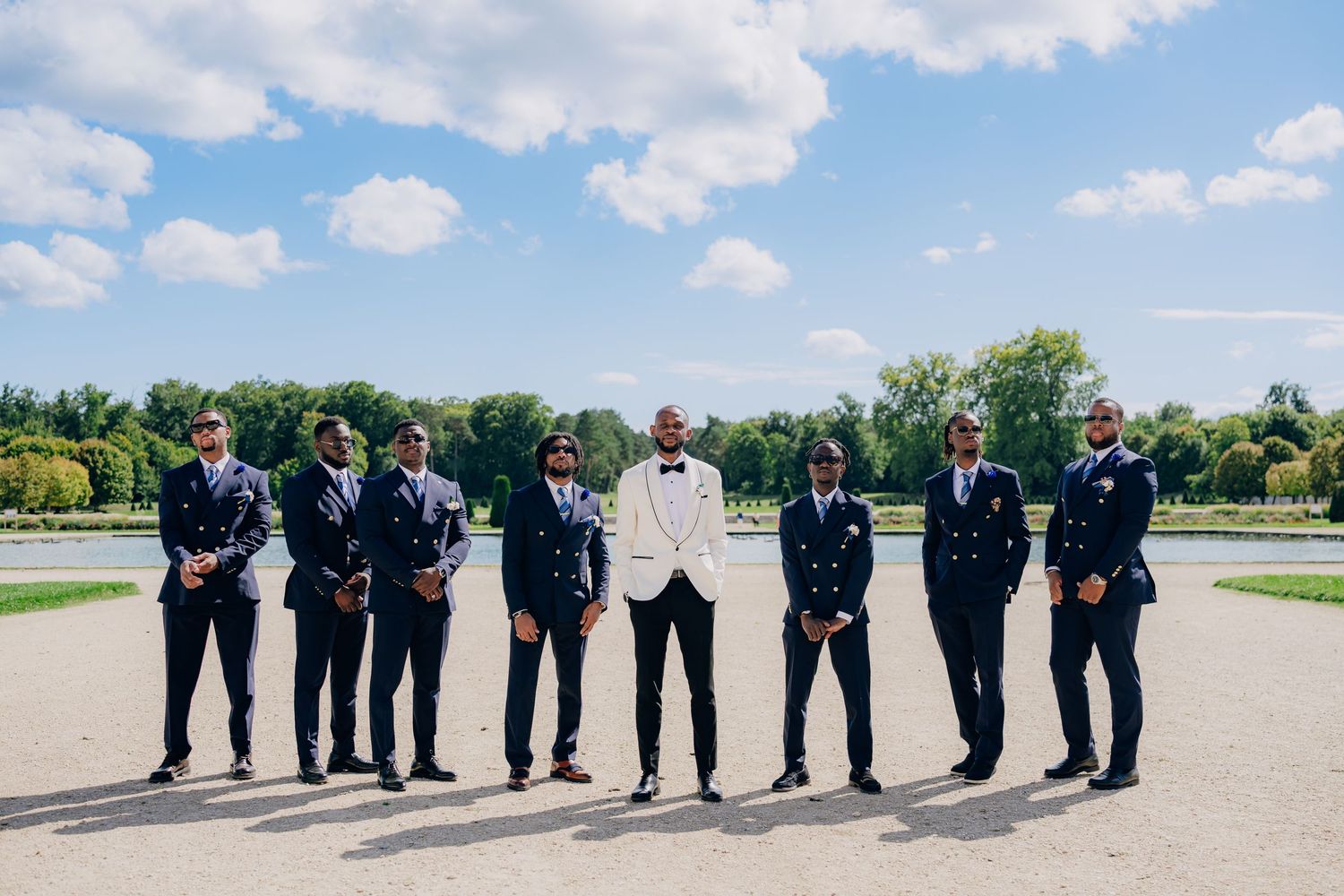 Wedding party members line up for creative panoramic photo shoot against blue sky and green landscape.