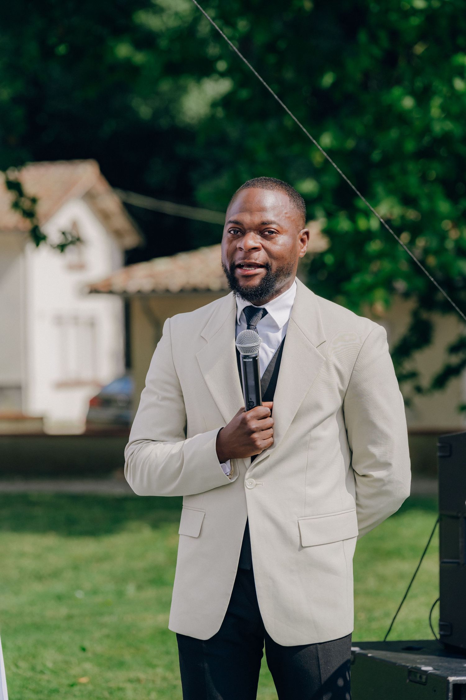 A speaker in a light colored suit jacket addresses an audience outdoors on a sunny day.