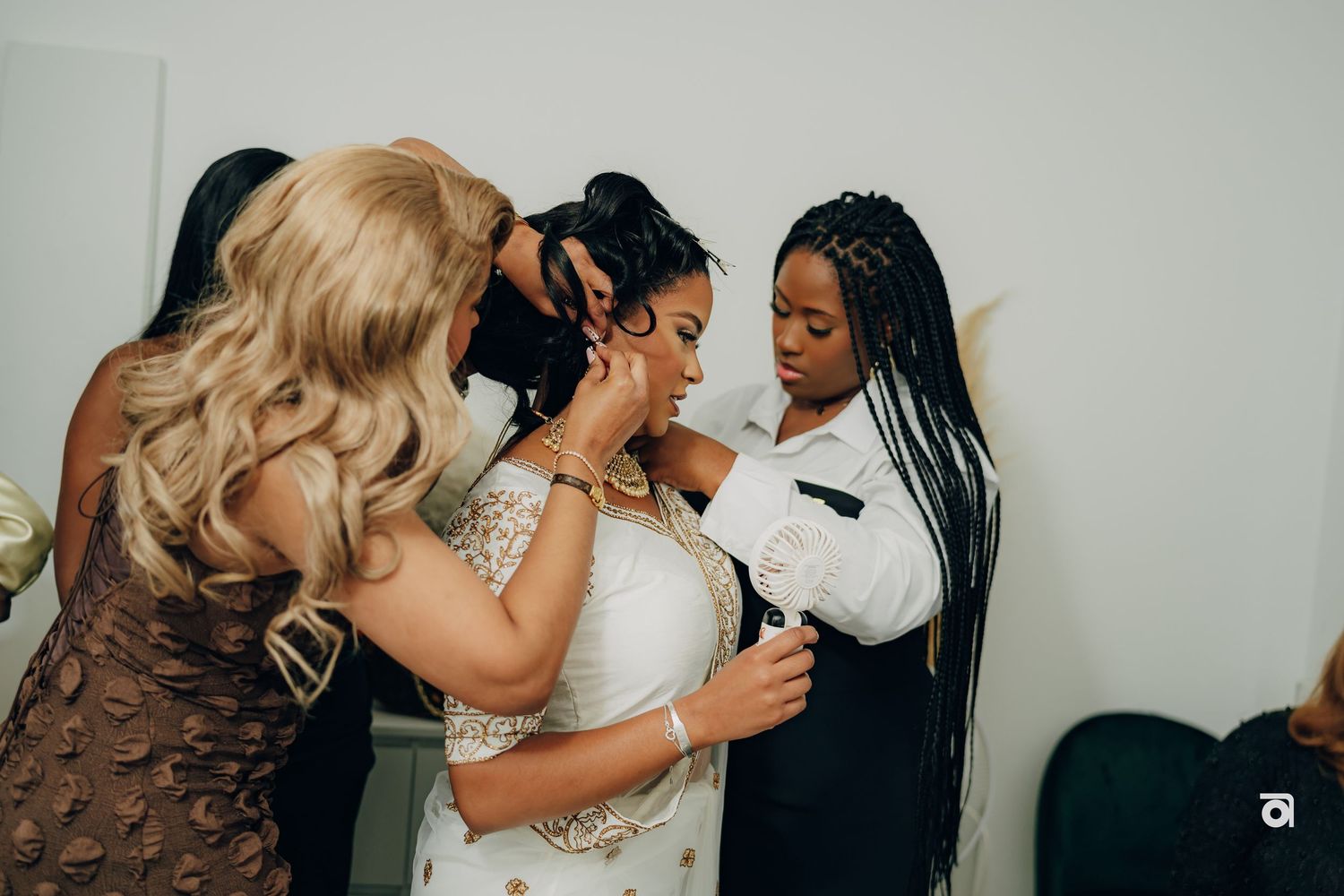 Wedding guests help adjust the bride's dress during preparation moments at a modern indoor celebration.