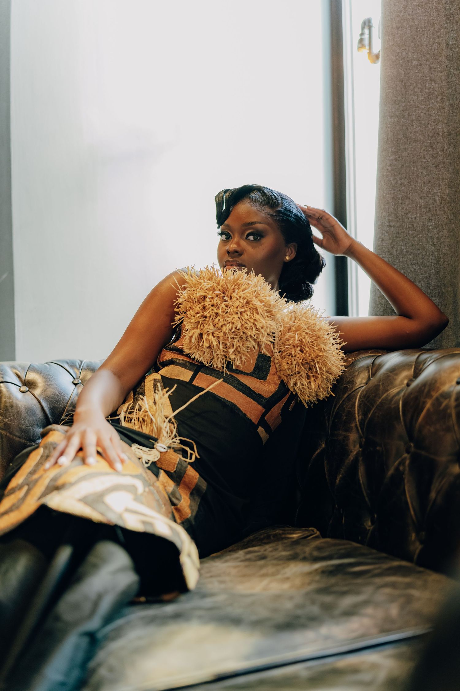 A person in black dress lounges on a leather couch holding a fluffy tan-colored teddy bear.
