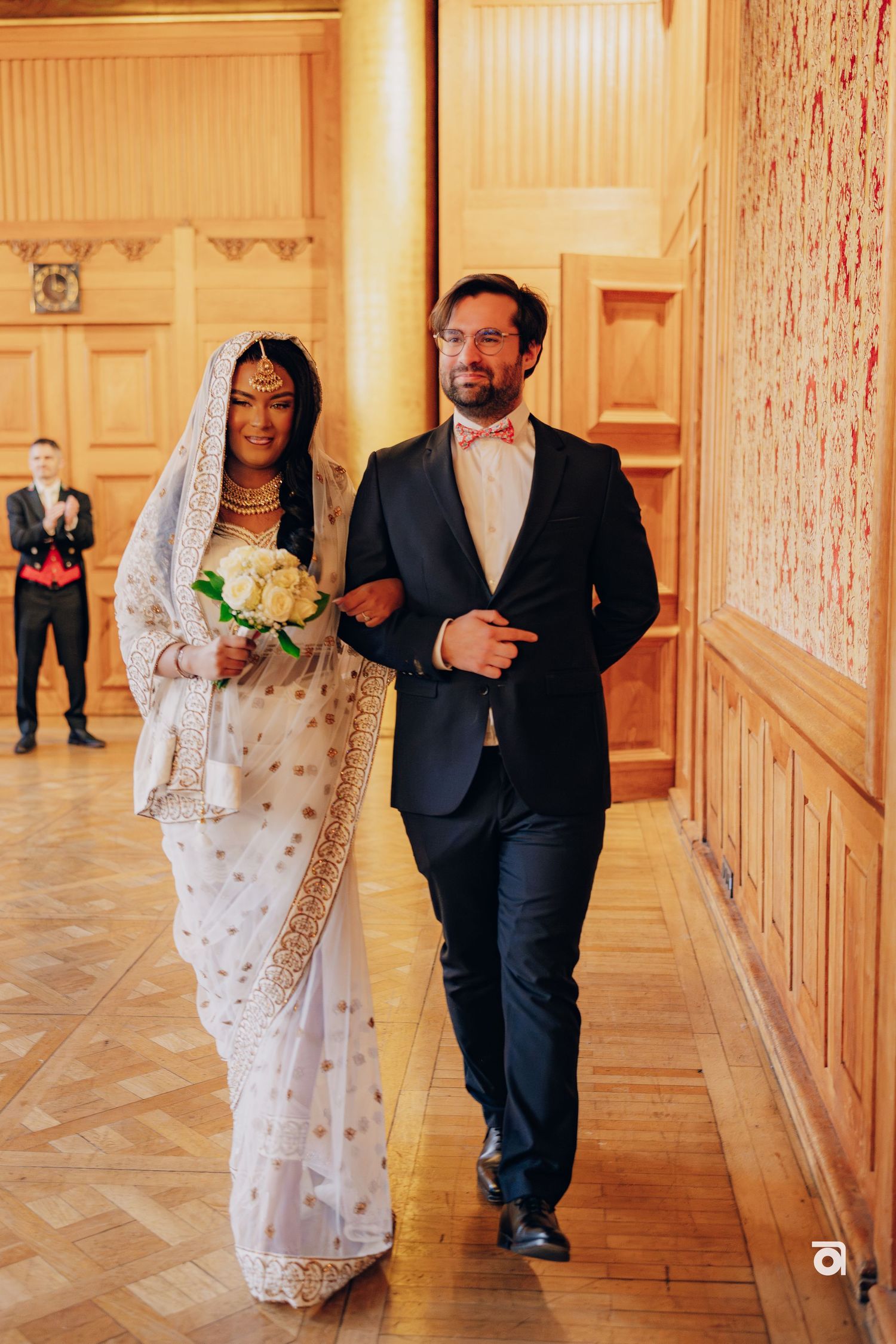 A couple walks down an elegant hallway with wood paneling and parquet floors during their wedding ceremony.