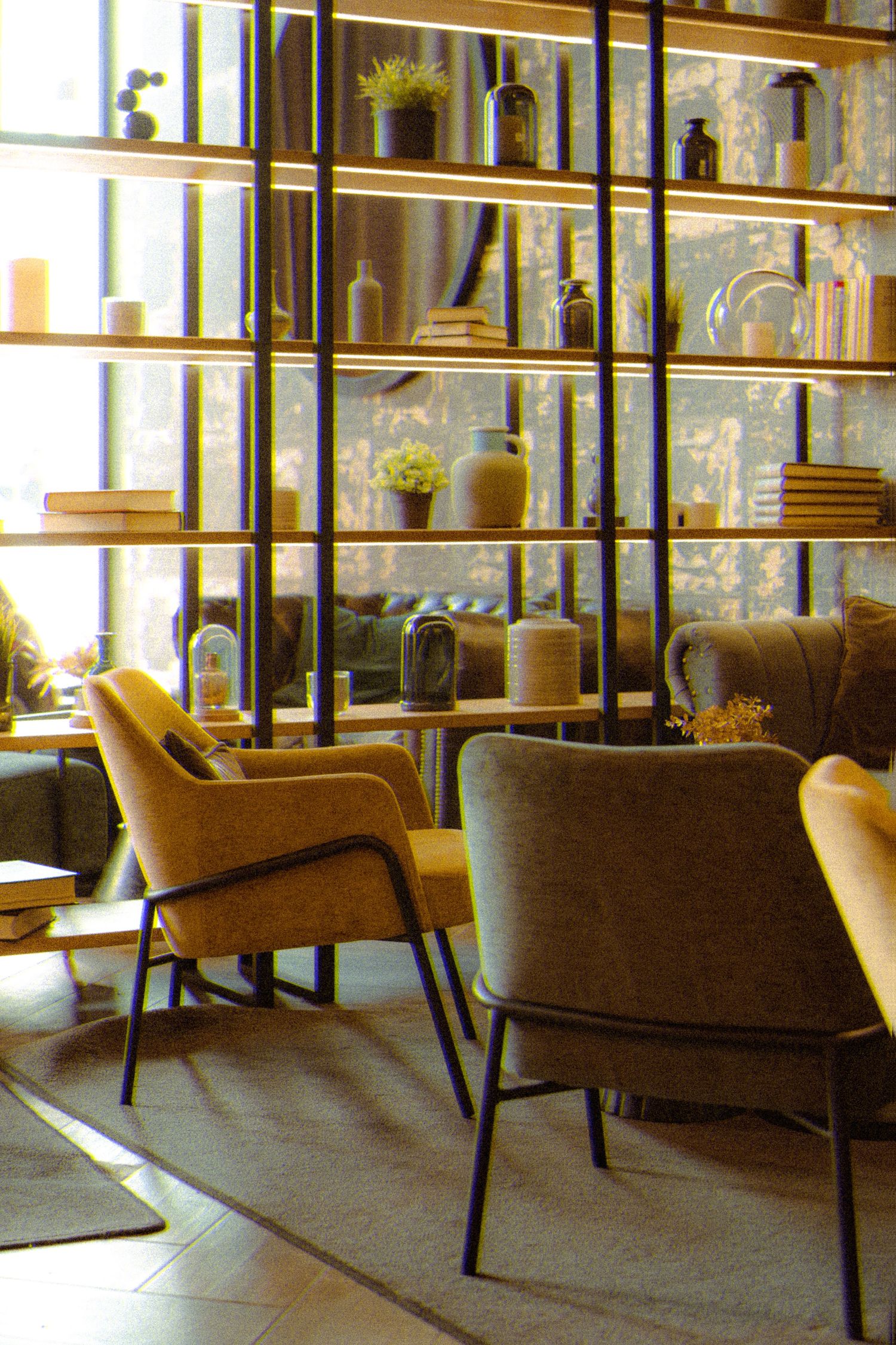 Modern interior with mid-century armchairs and wooden shelving unit displaying decorative bottles and objects in warm lighting.