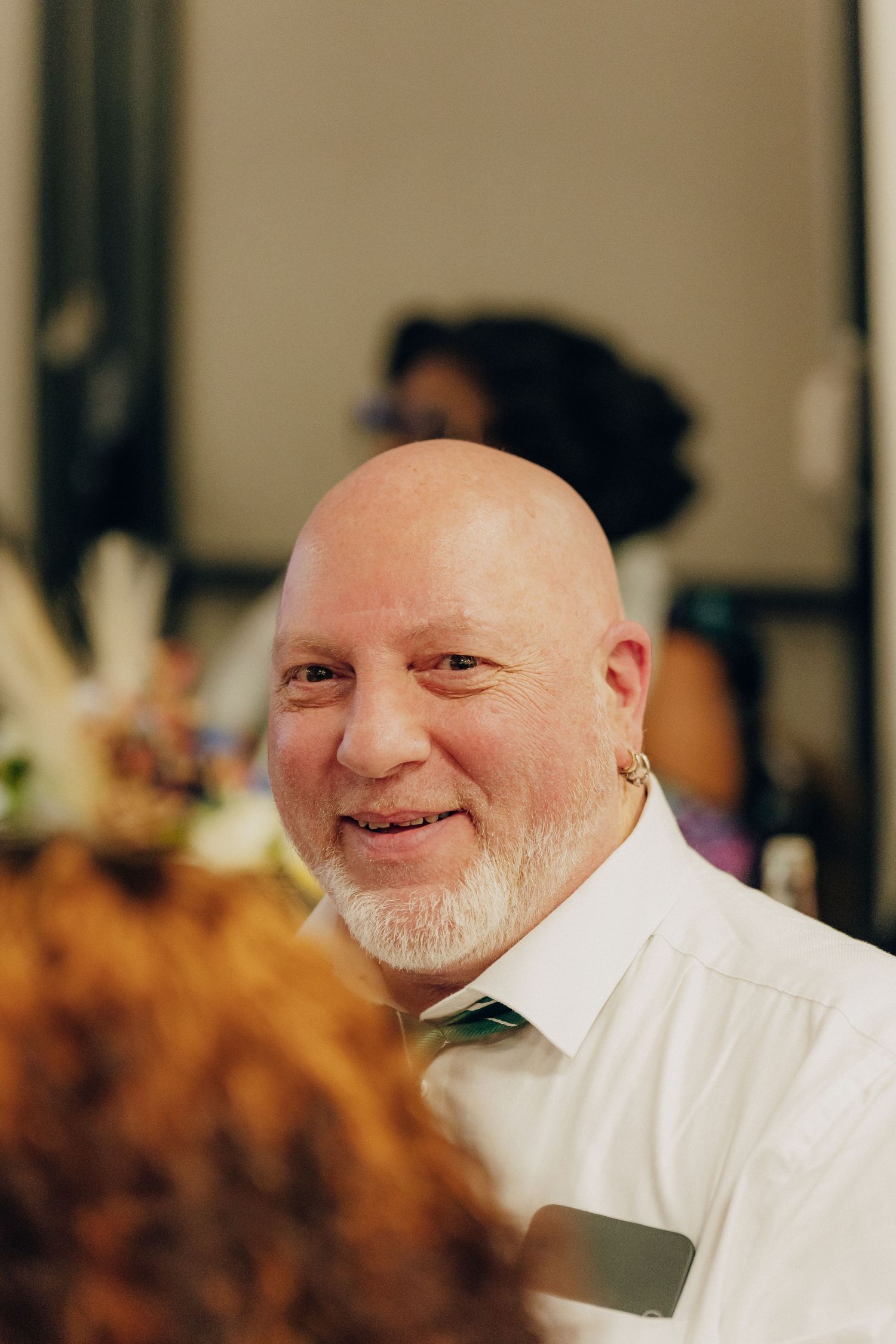 A person in a white dress shirt smiles warmly at a social gathering.