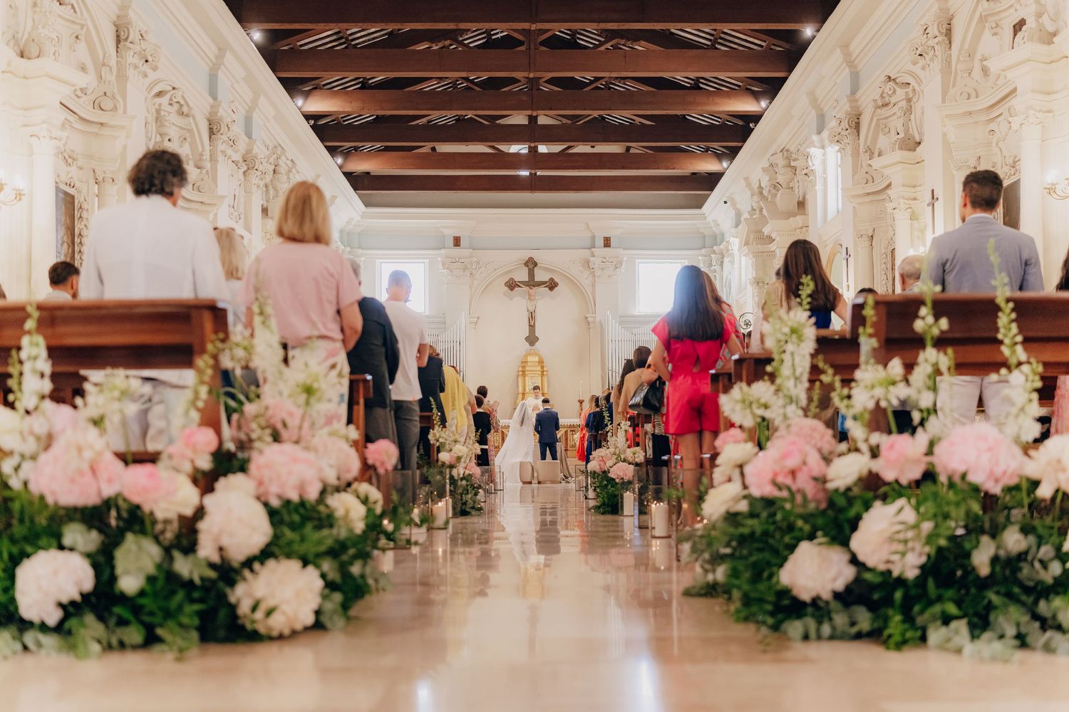 Elegant wedding venue decorated with lush white floral arrangements and greenery along the aisle and altar area.
