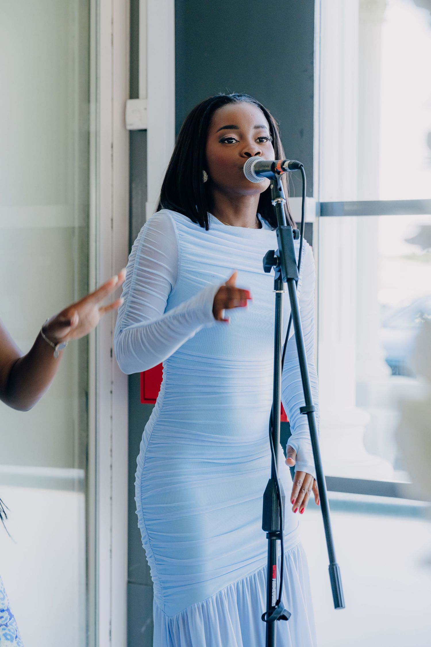 Singer in a white long-sleeved dress performs with a microphone during what appears to be a wedding ceremony.