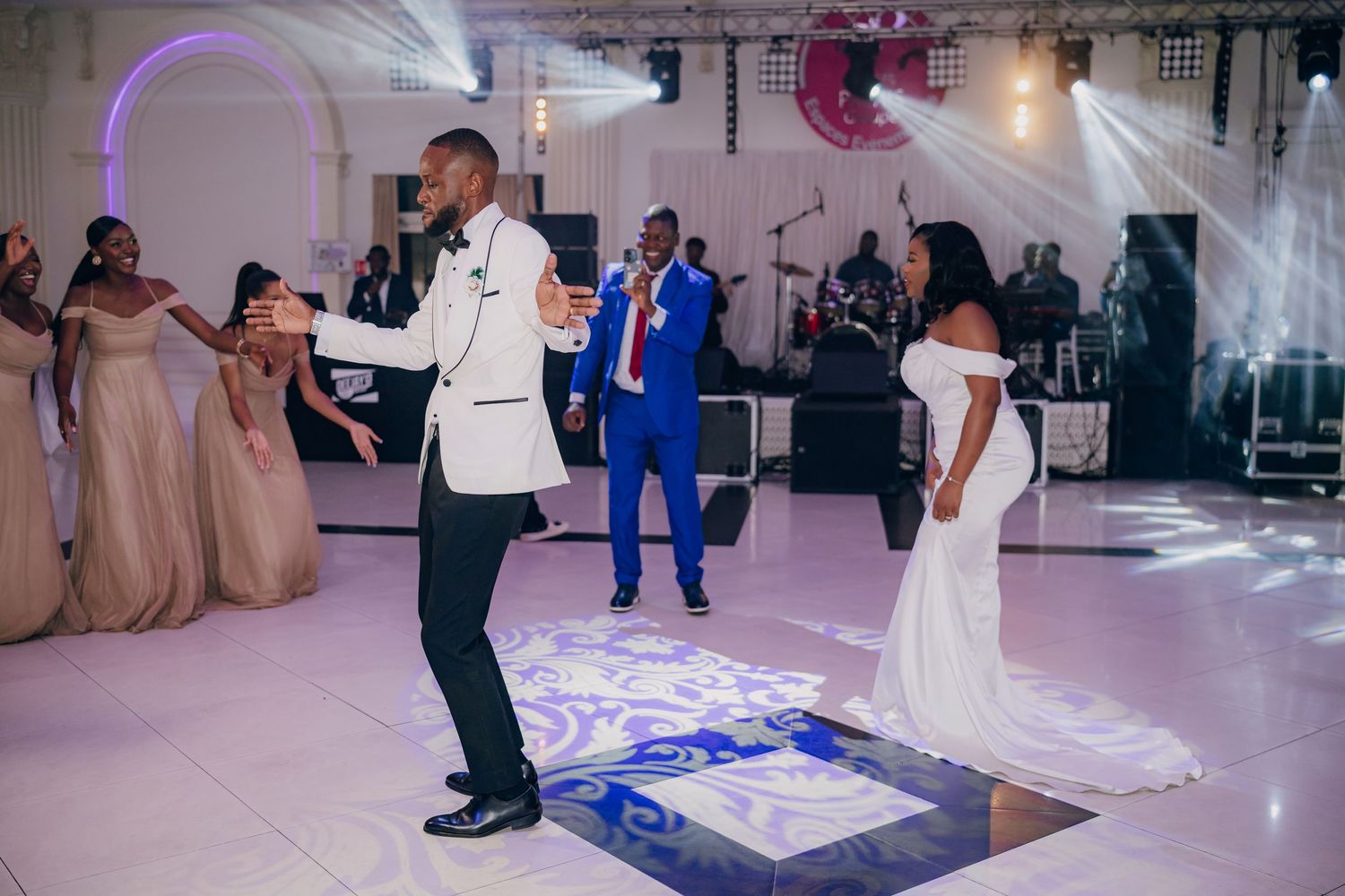Guests dancing and celebrating at a wedding reception in an elegant ballroom with purple lighting effects.